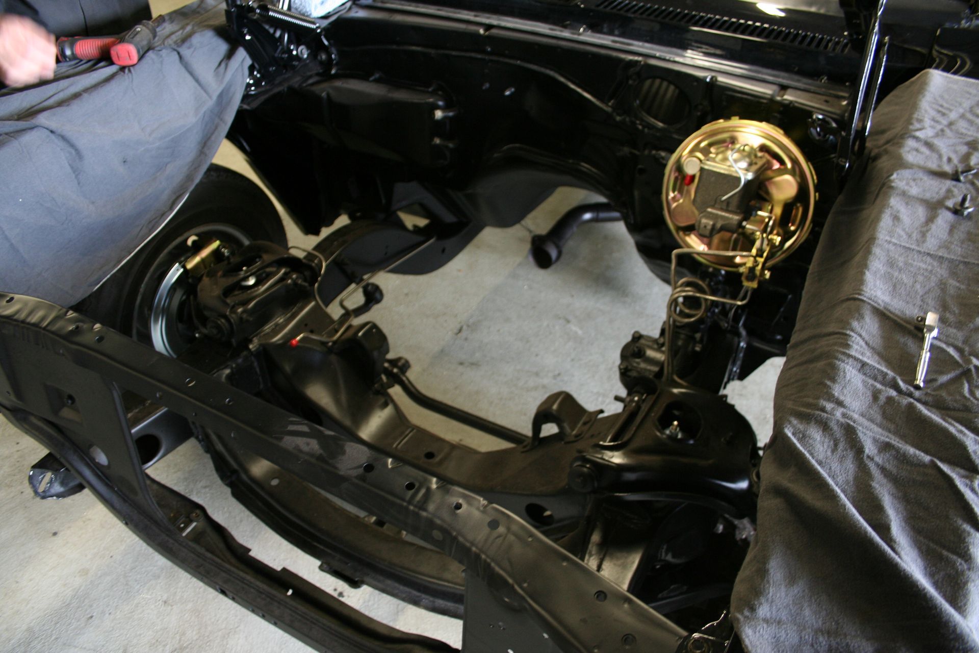 Black car frame with gold brake booster being worked on, in a garage. | Autobahn Performance Inc