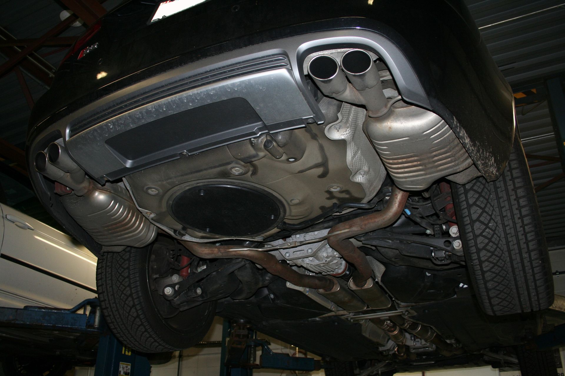 Undercarriage of a black car lifted on a hoist, showing exhaust system with dual mufflers. | Autobahn Performance Inc