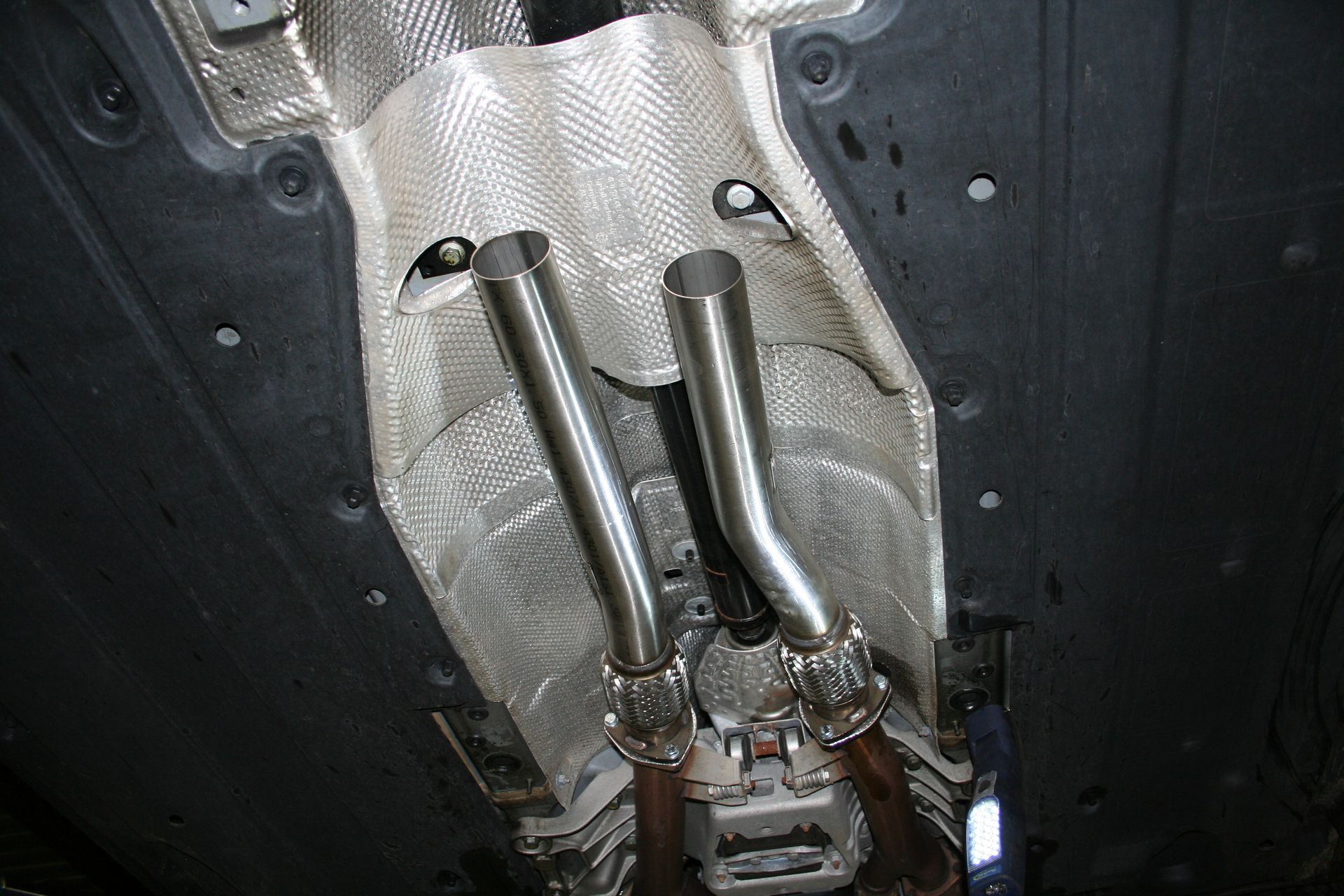 Underside of a car showing two shiny exhaust pipes and heat shielding. | Autobahn Performance Inc