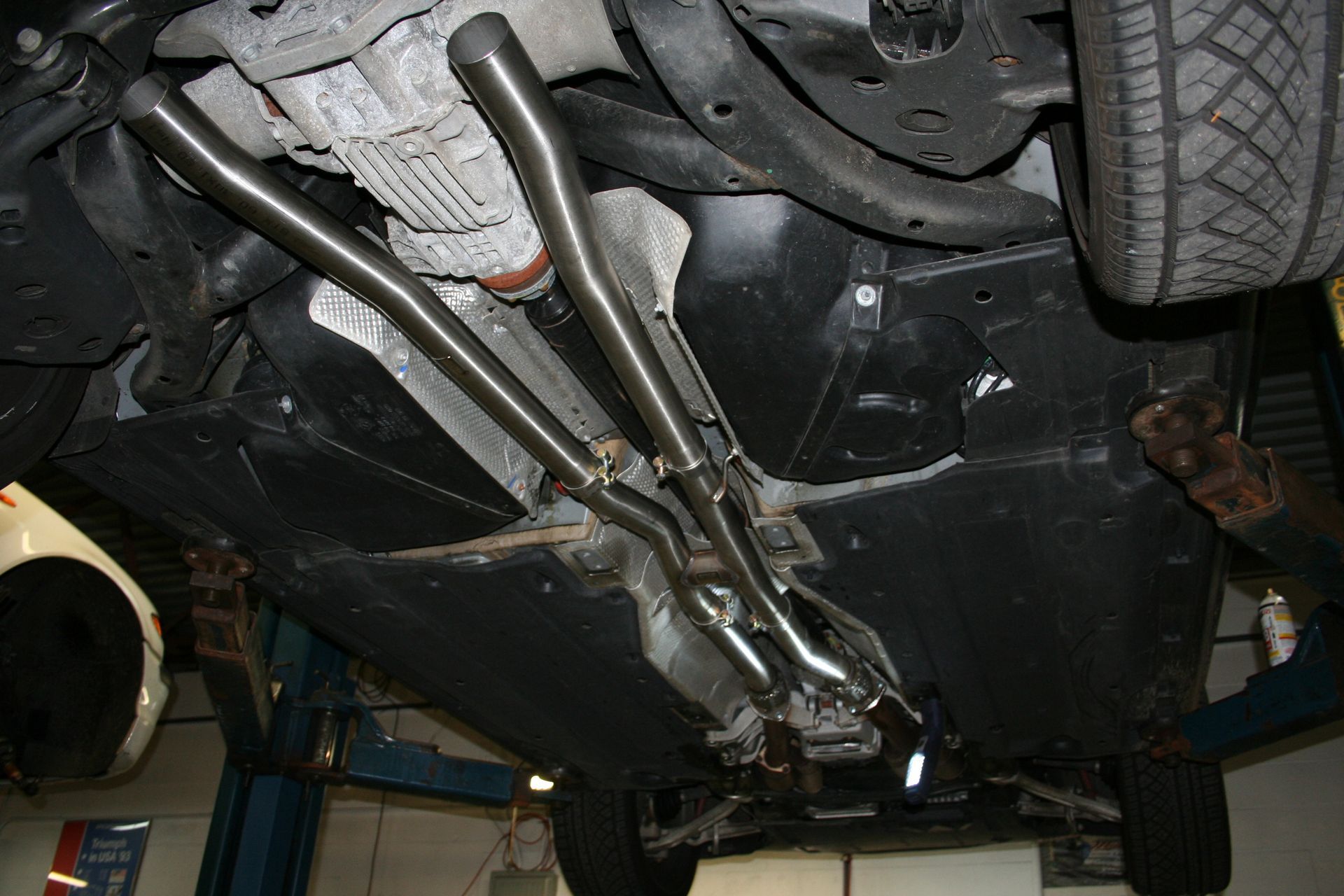 Underside of a car with custom exhaust pipes visible. The vehicle is on a lift. | Autobahn Performance Inc