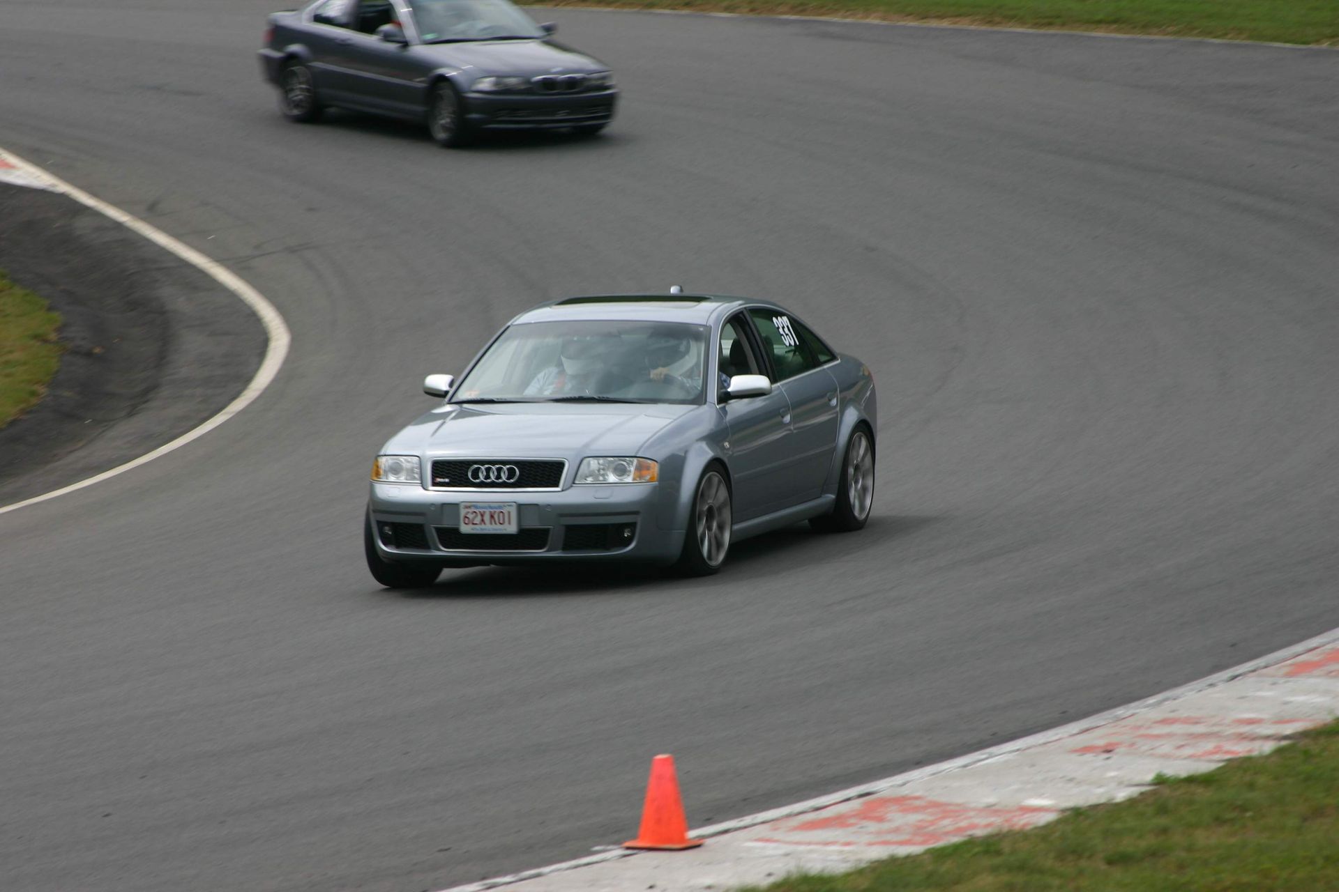Silver Audi sedan racing on a track, orange cone, with a dark blue BMW following. | Autobahn Performance Inc