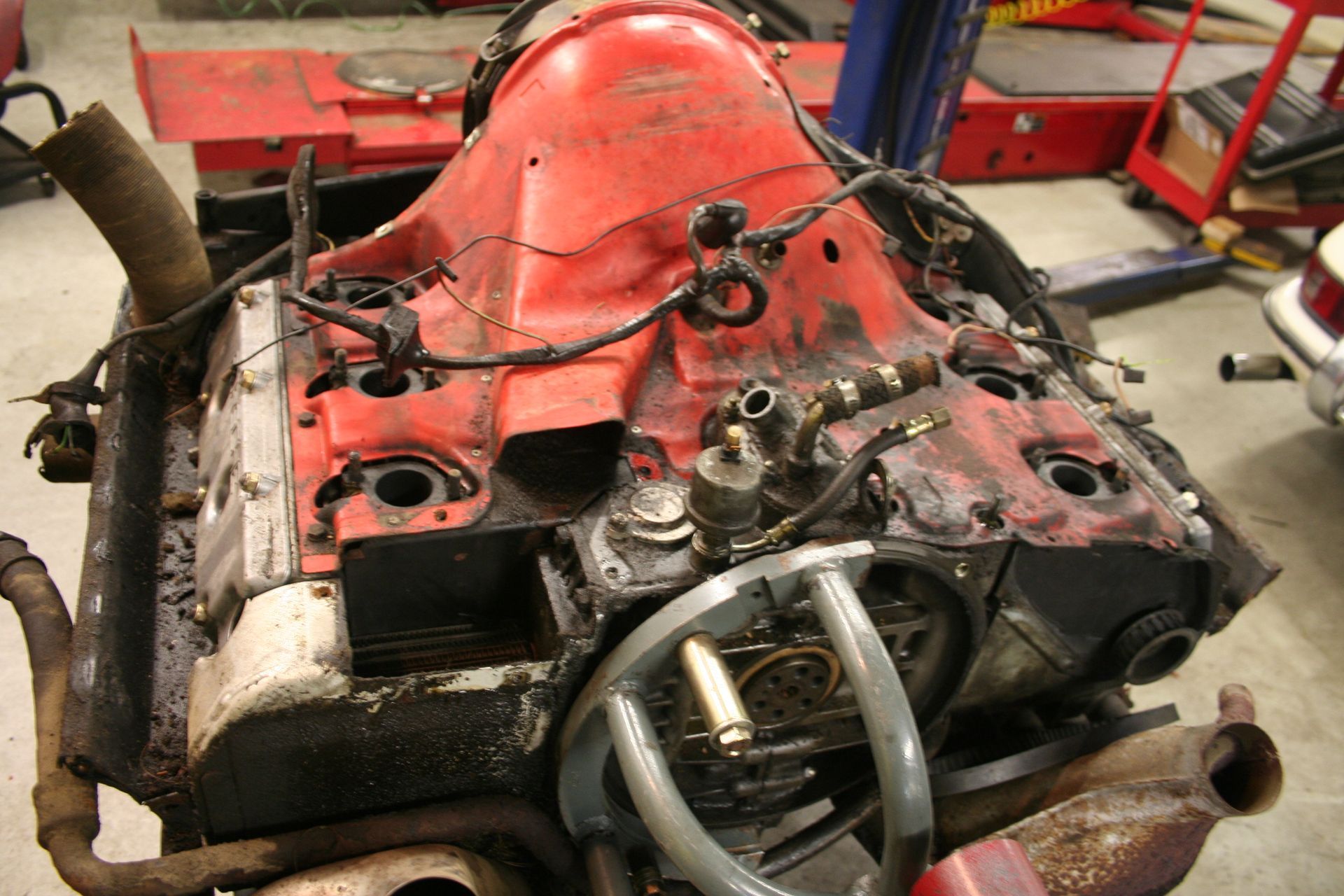 A disassembled car engine in a repair shop; red frame, black engine components, and various tools. | Autobahn Performance Inc