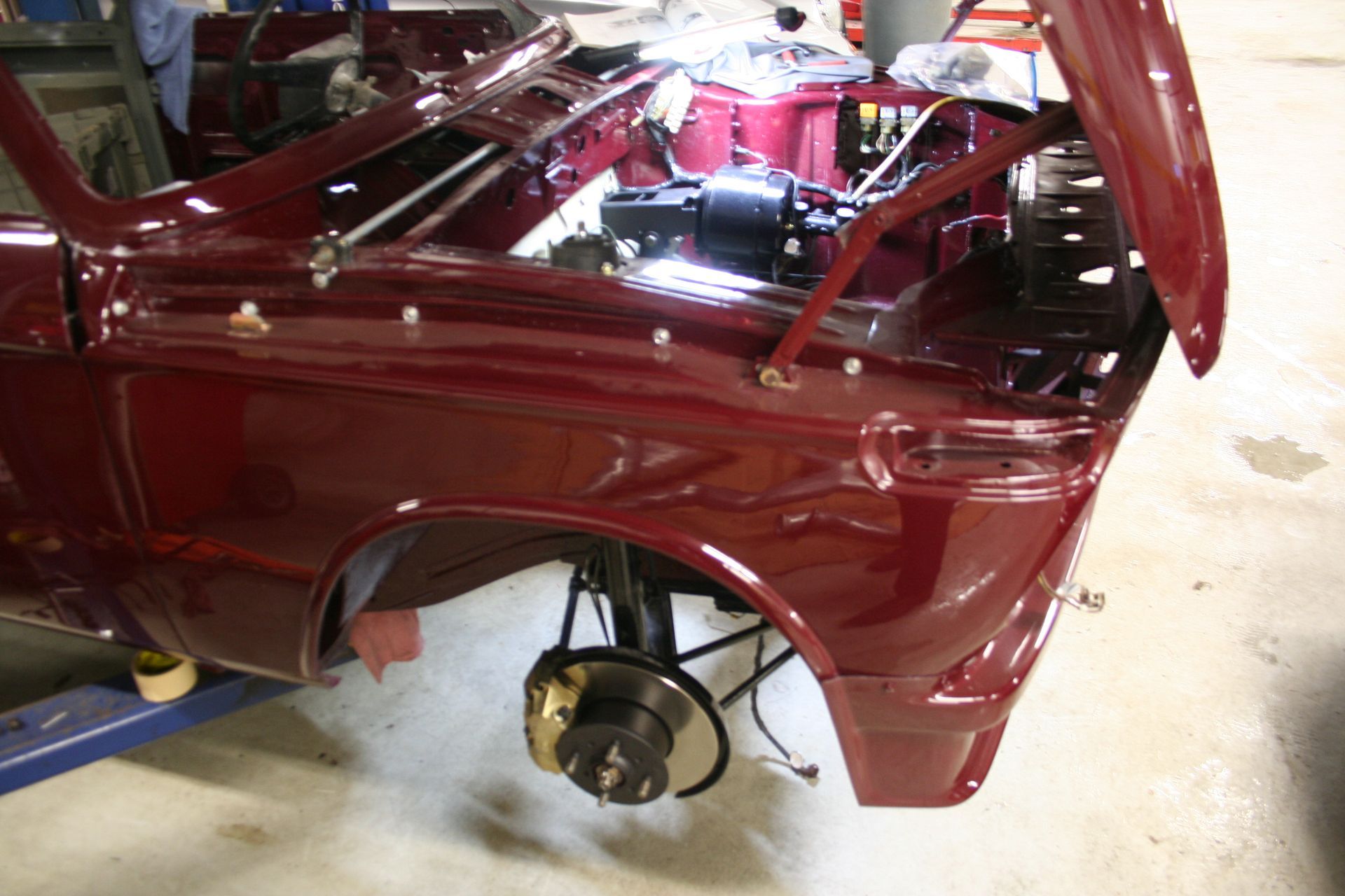 Burgundy car's front with open hood, showing engine components and front suspension, being worked on in a shop. | Autobahn Performance Inc