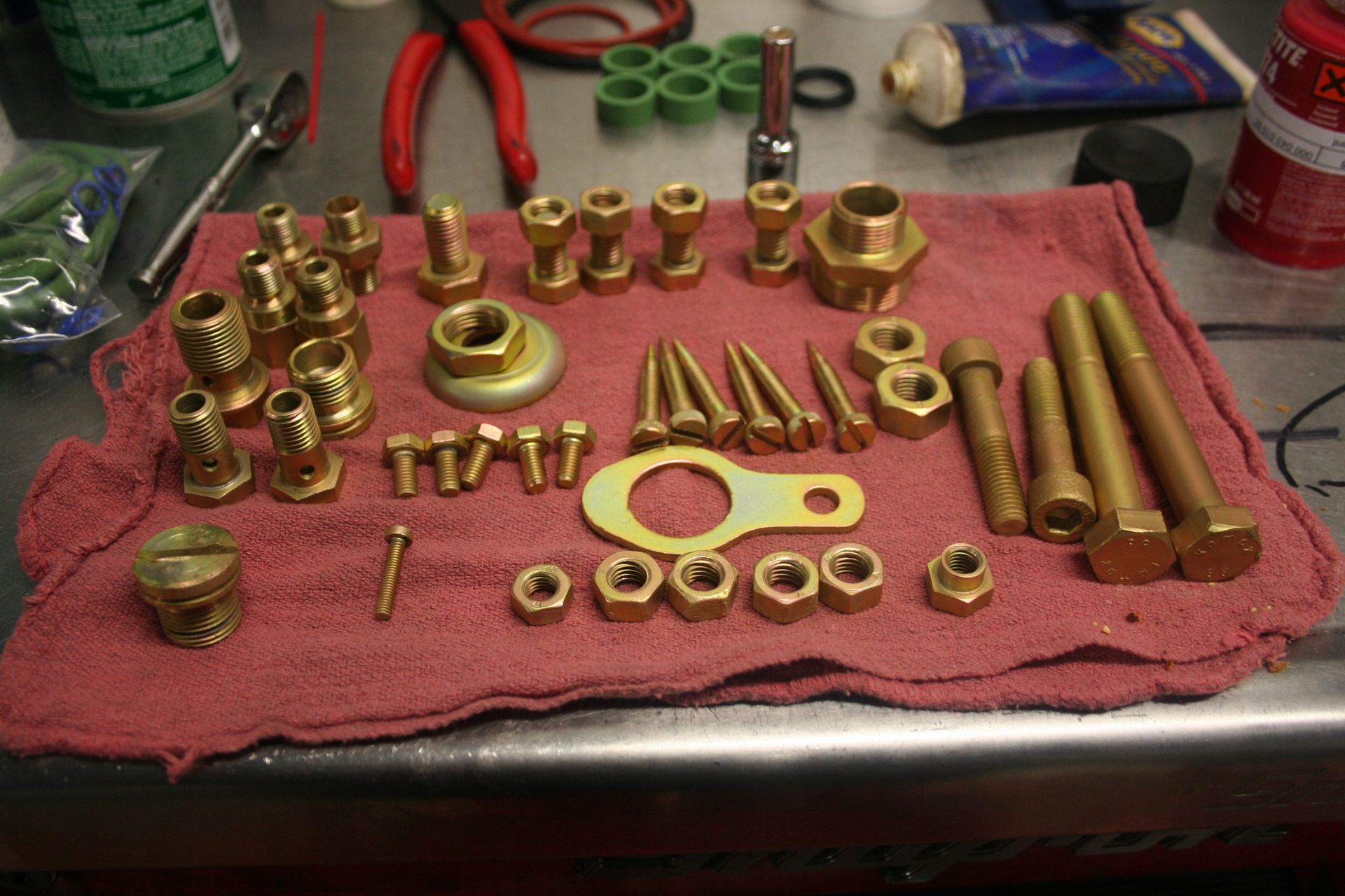 Brass fittings, bolts, and nuts arranged on a red cloth. Tools and other hardware are in the background. | Autobahn Performance Inc