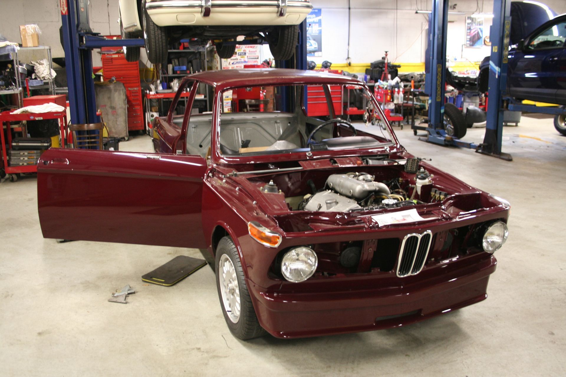 Burgundy BMW 2002 in a shop, doors open, engine visible, on a lift. | Autobahn Performance Inc