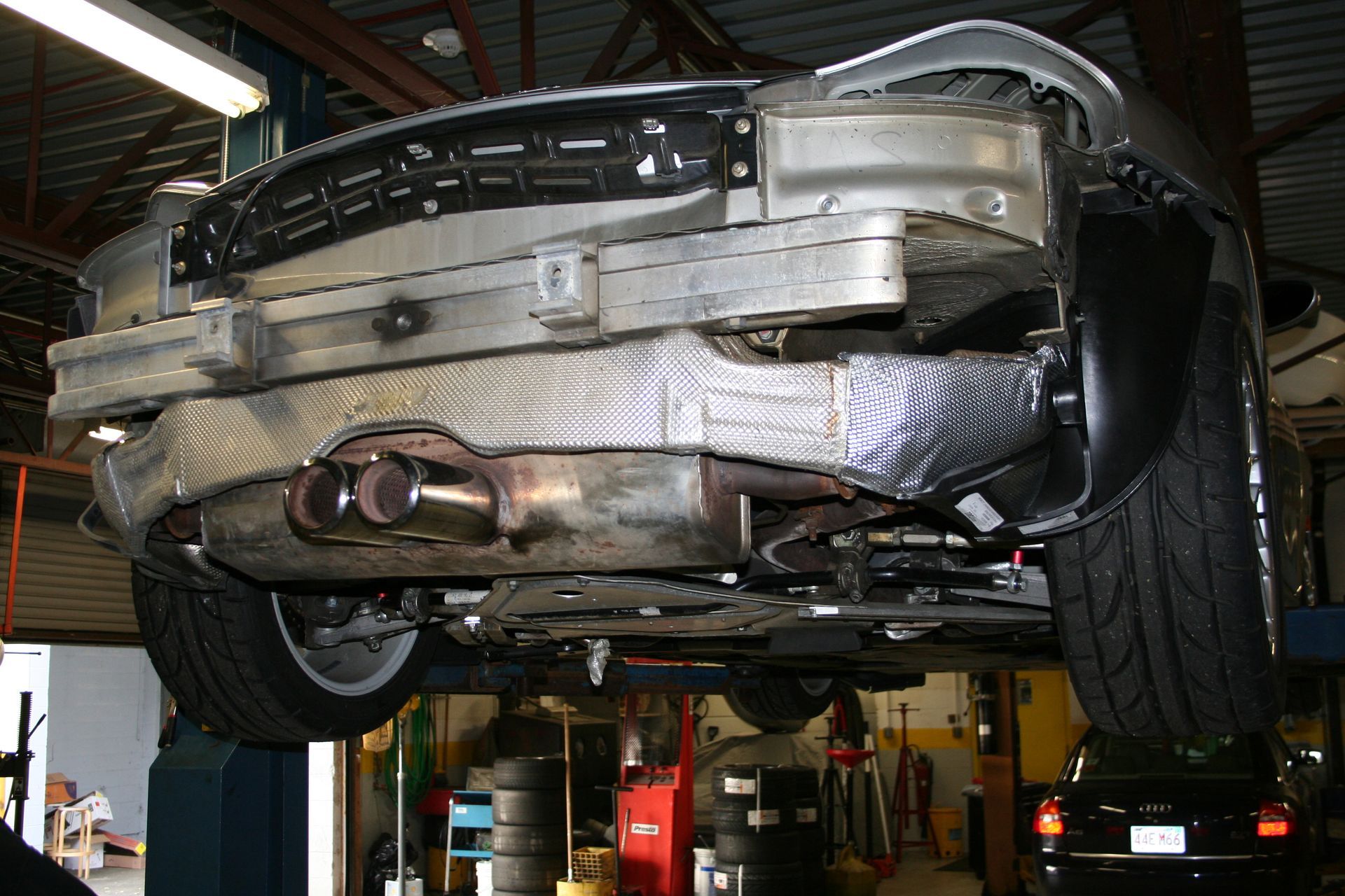 Underside view of a car raised on a lift in a garage; exhaust pipes, tires visible. | Autobahn Performance Inc