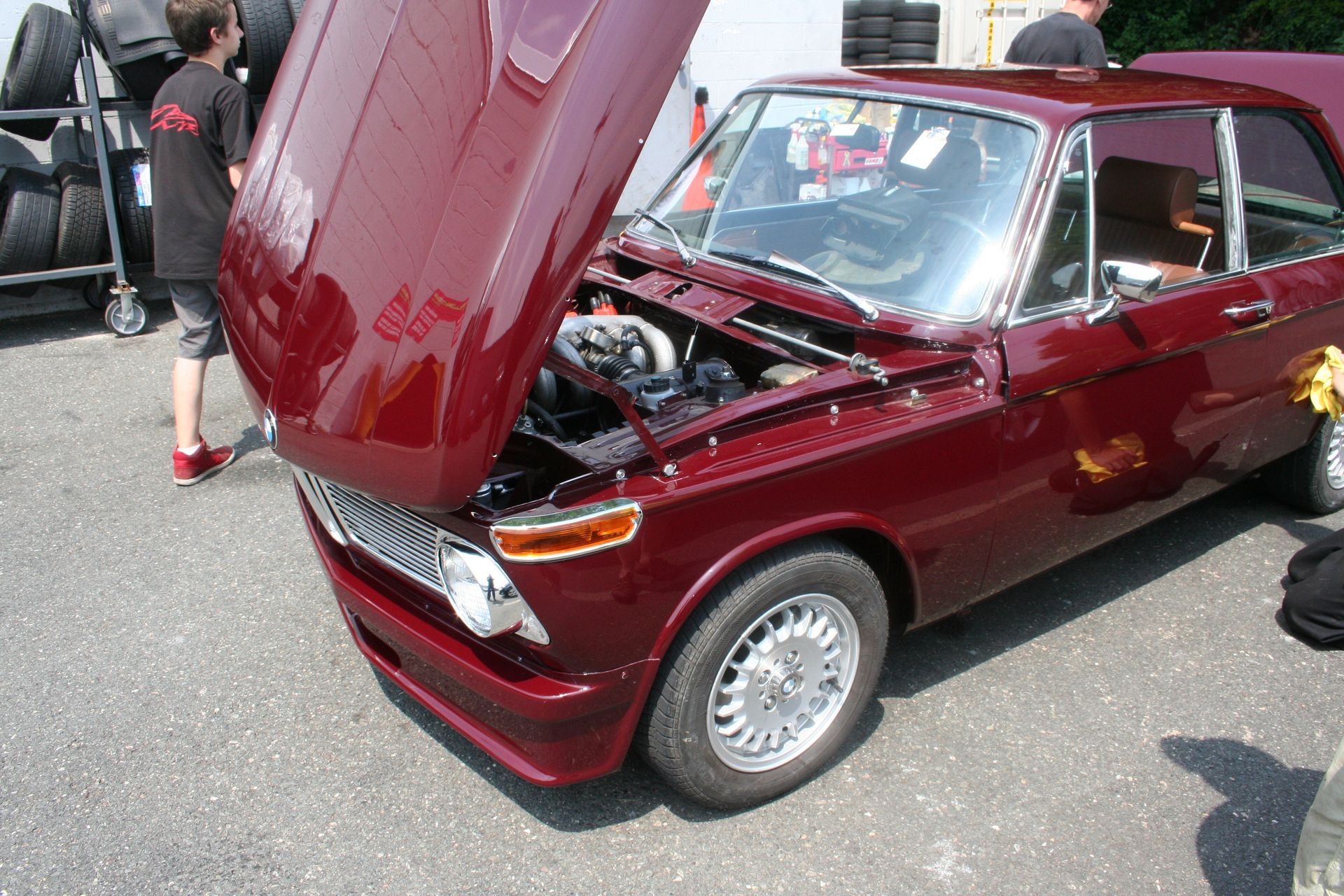 Burgundy BMW 2002 with open hood at an outdoor car show. | Autobahn Performance Inc