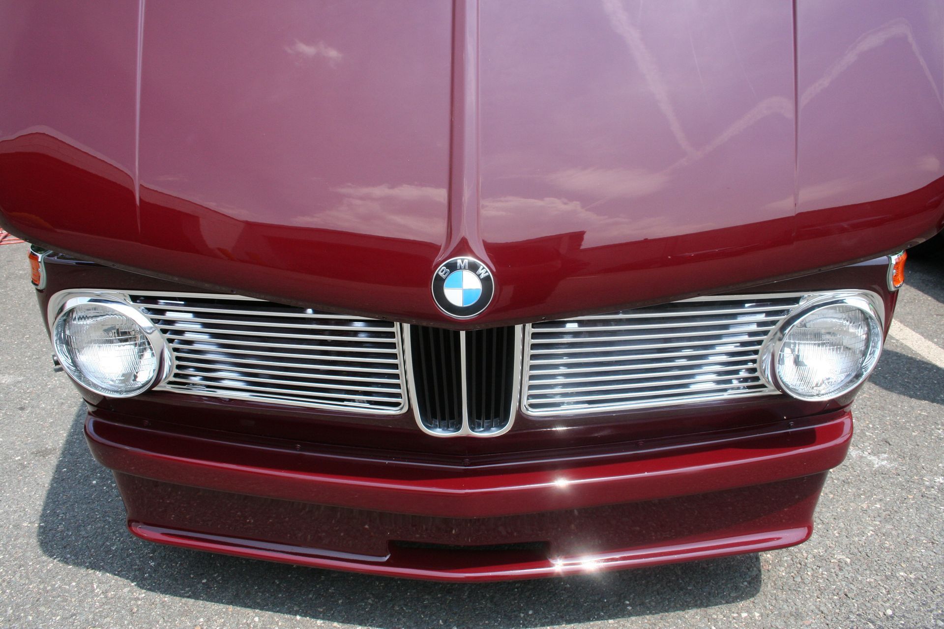Close-up of a burgundy BMW 2002's front, showing the hood, grill, headlights, and bumper. | Autobahn Performance Inc