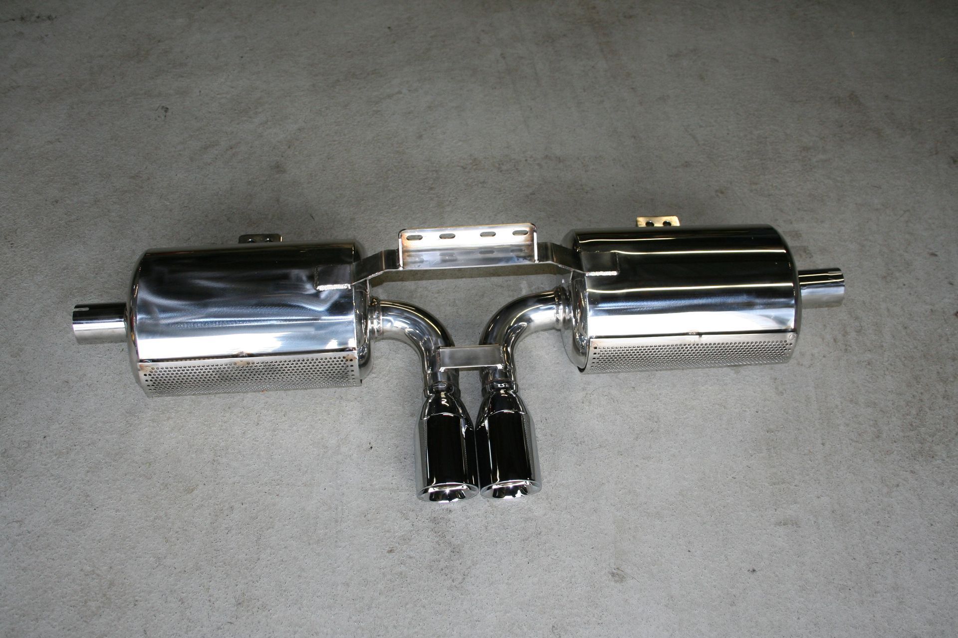 Polished stainless steel car exhaust system on a concrete surface with two mufflers, dual tips, and connecting pipes. | Autobahn Performance Inc