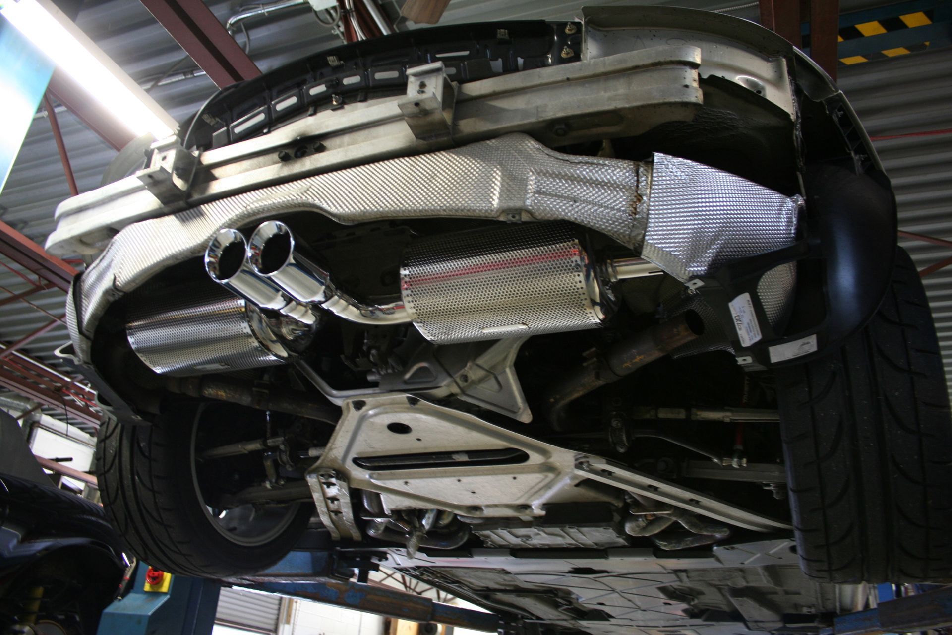 Underside of a car on a lift, showing exhaust system and rear suspension details. | Autobahn Performance Inc