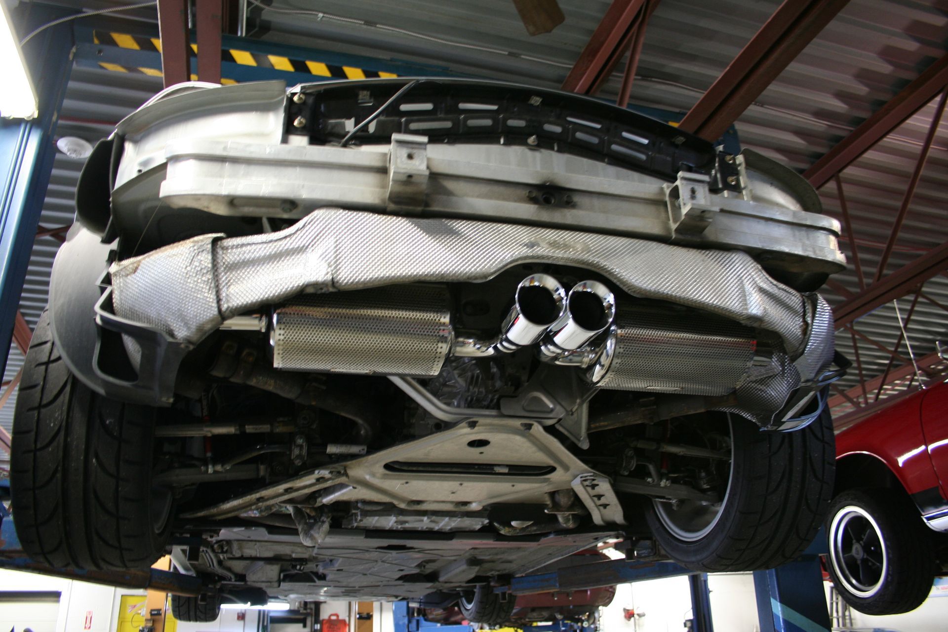 Underside of a silver sports car raised on a lift in a garage, showcasing exhaust system and undercarriage. | Autobahn Performance Inc