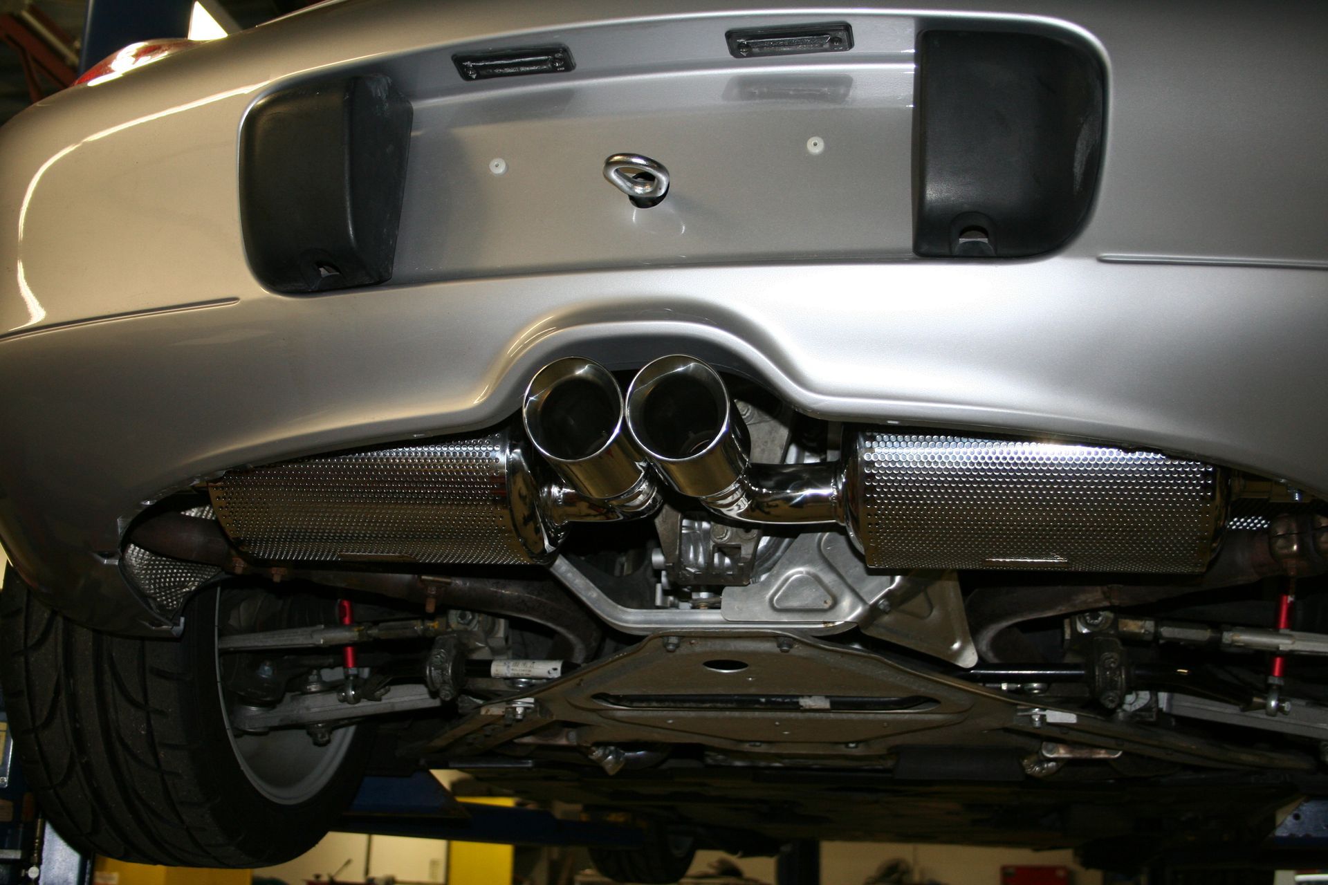 Silver car's undercarriage showing dual exhaust pipes, carbon fiber panels, and suspension components. | Autobahn Performance Inc