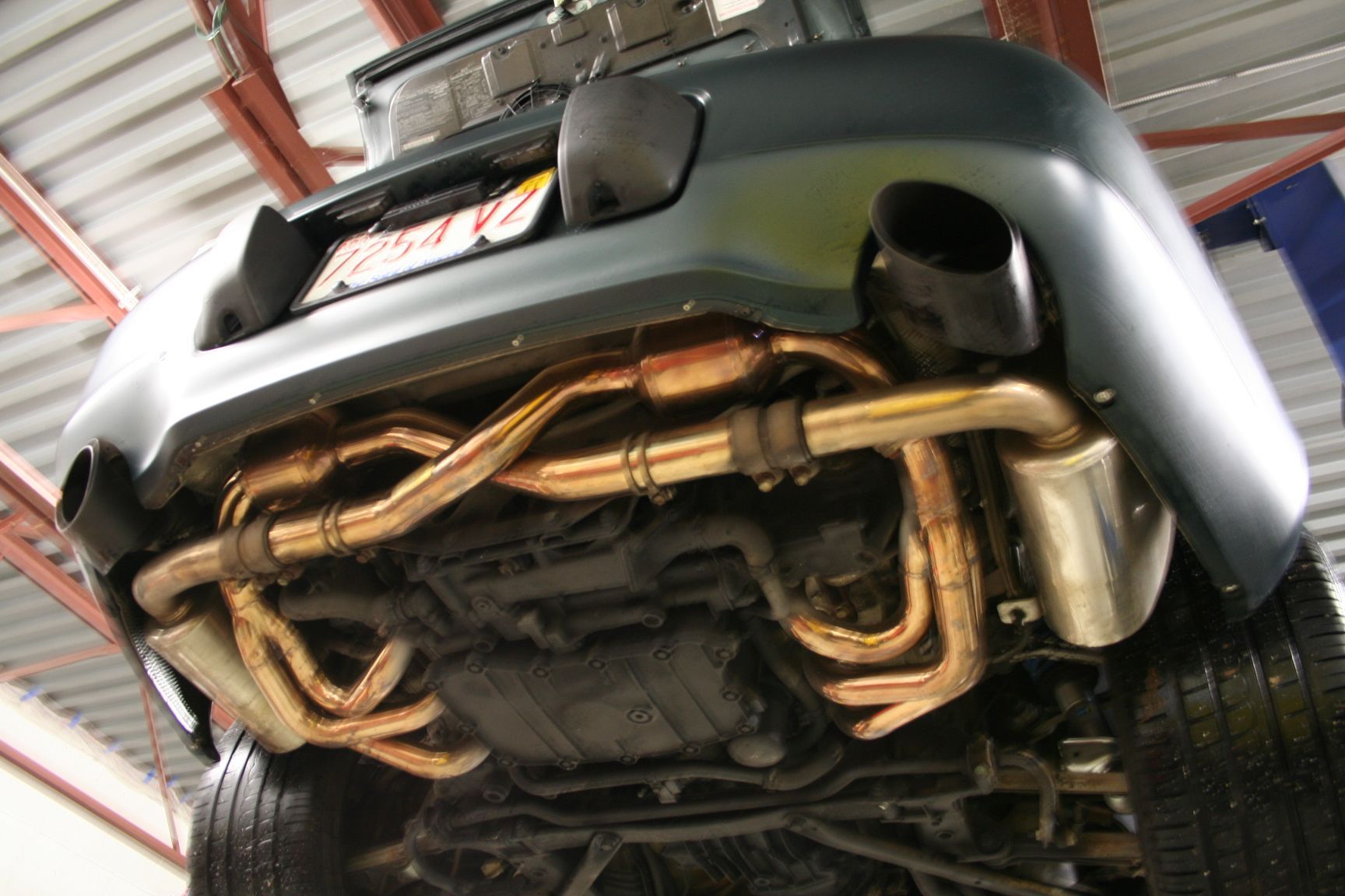 Underside view of a car with an upgraded golden exhaust system, visible from rear bumper. | Autobahn Performance Inc