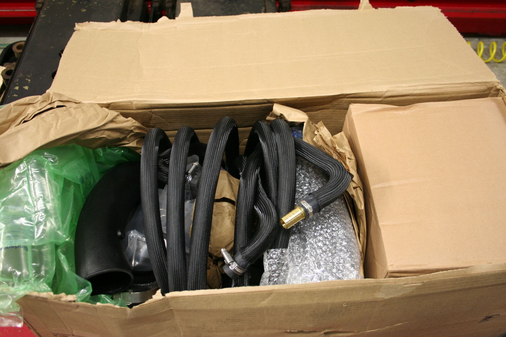 Open cardboard box containing automotive parts, including hoses and a black intake tube. | Autobahn Performance Inc