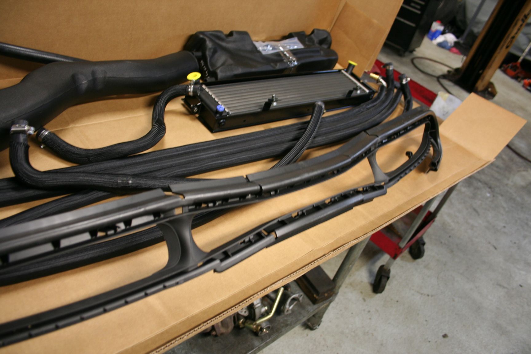 Parts of a car's cooling system in a cardboard box, including hoses, a radiator, and a black trim piece. | Autobahn Performance Inc