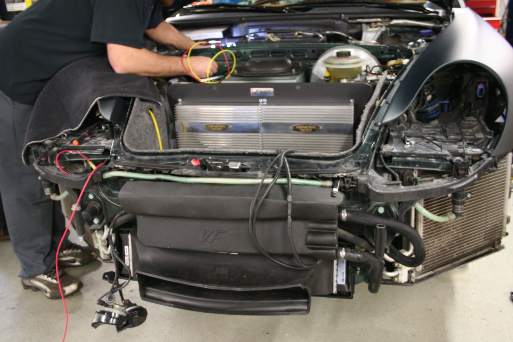Mechanic working on the engine of a dark green car with the front end disassembled. | Autobahn Performance Inc