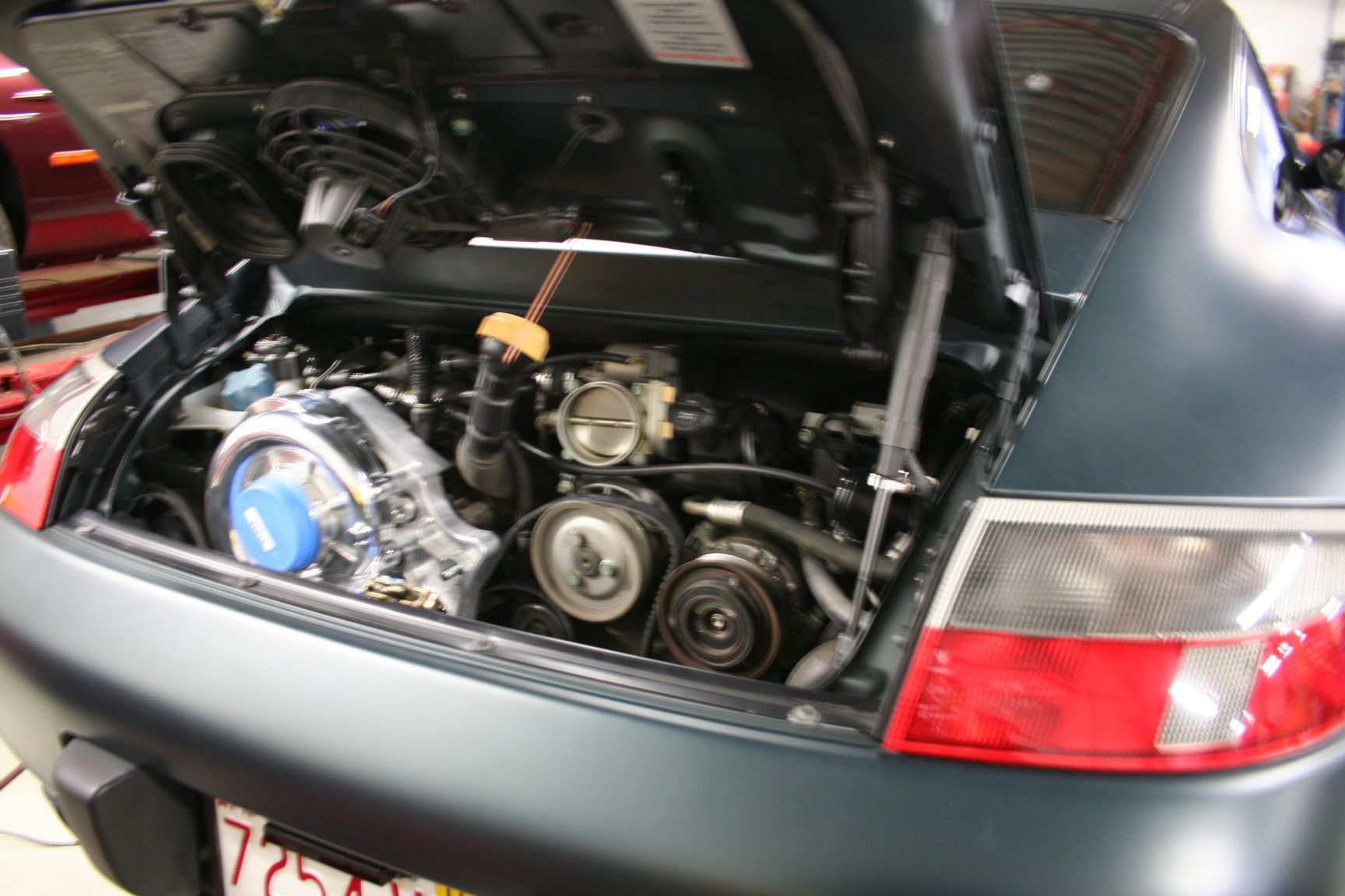 Engine bay of a dark blue Porsche 911 with the trunk open, revealing engine components. | Autobahn Performance Inc