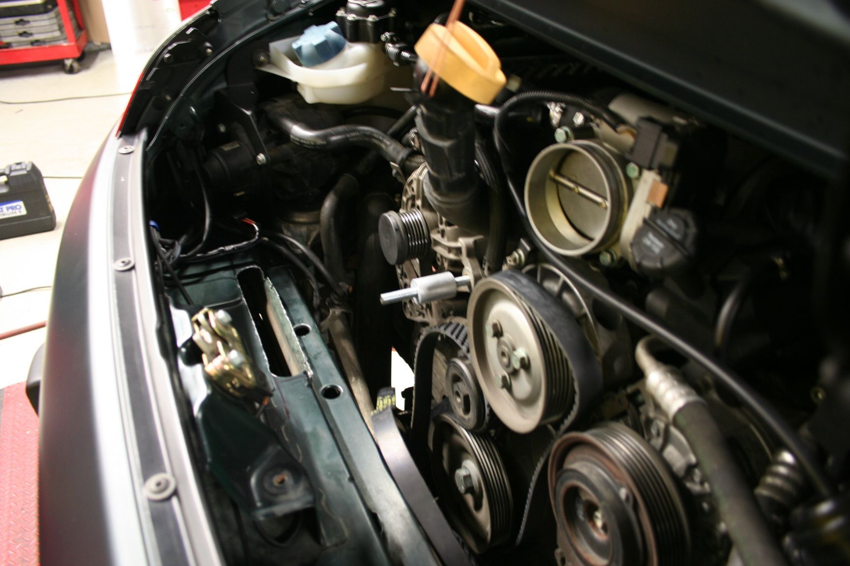 Engine bay of a black vehicle, showing belts, pulleys, and various mechanical components. | Autobahn Performance Inc