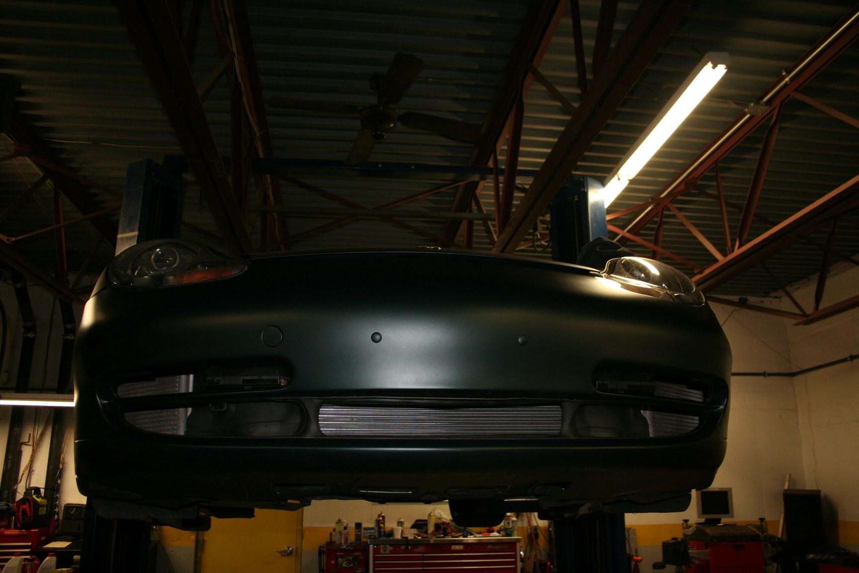 Green car on a lift in a garage, viewed from below, showing front end. | Autobahn Performance Inc