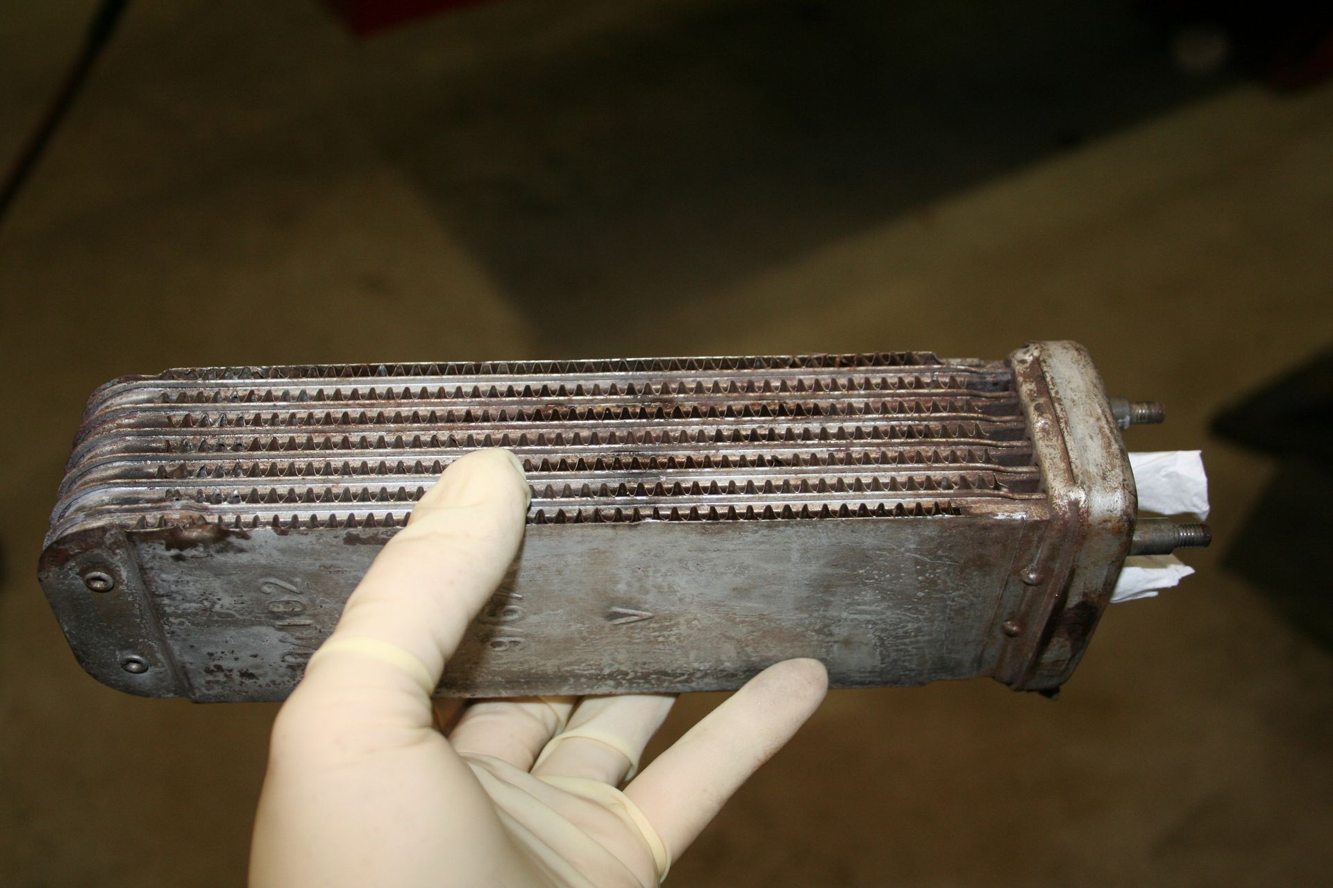 Gloved hand holding a corroded metal heat exchanger with fins, likely from a vehicle. | Autobahn Performance Inc