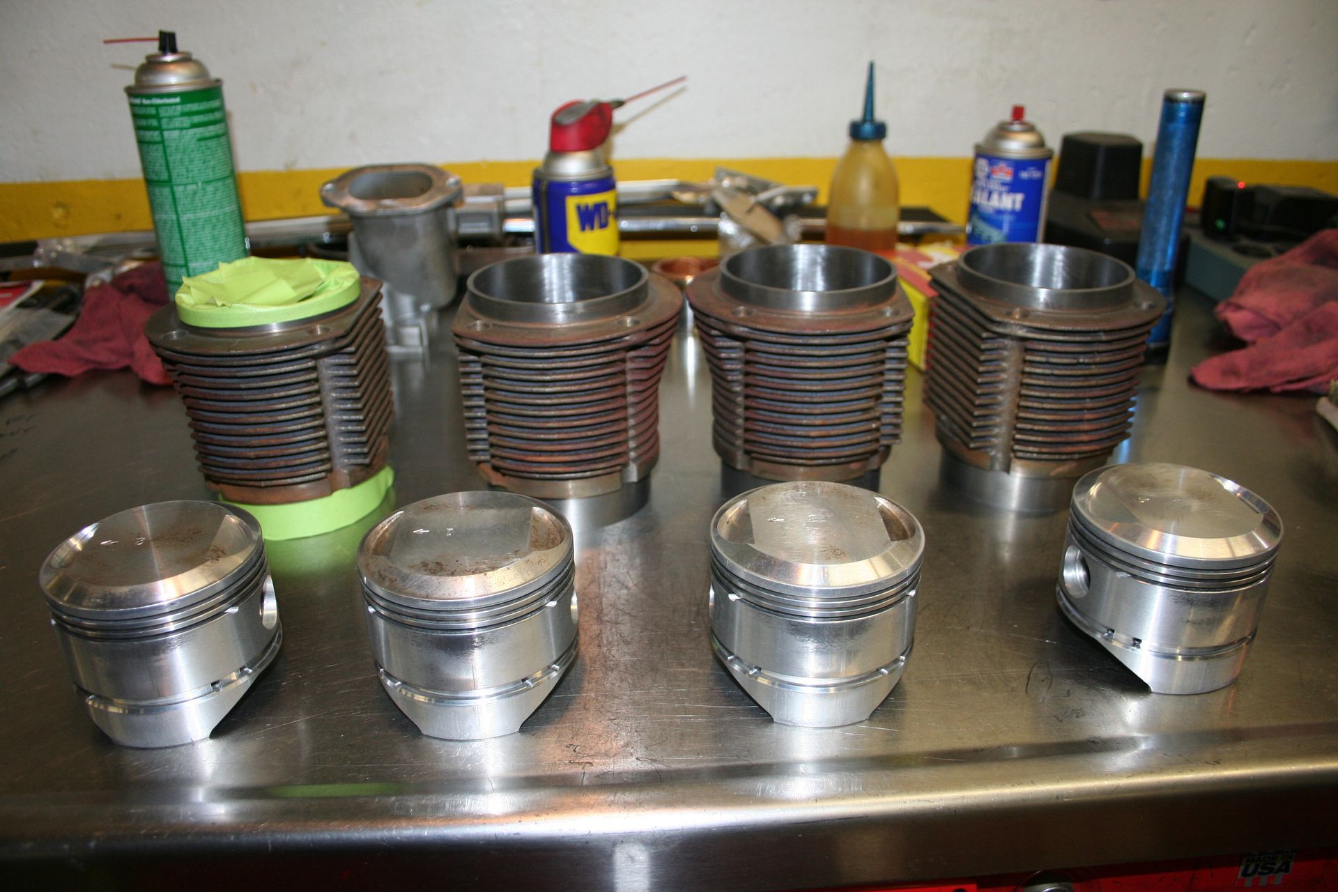 Engine cylinders and pistons on a work surface, workshop setting with various tools and supplies. | Autobahn Performance Inc