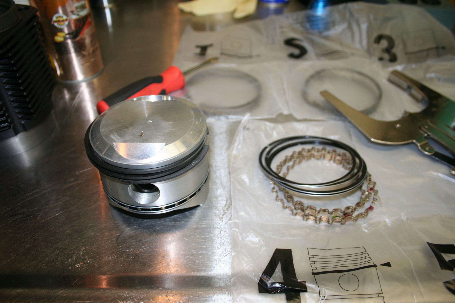 Piston with new rings and tools on a work surface, possibly for engine repair. | Autobahn Performance Inc