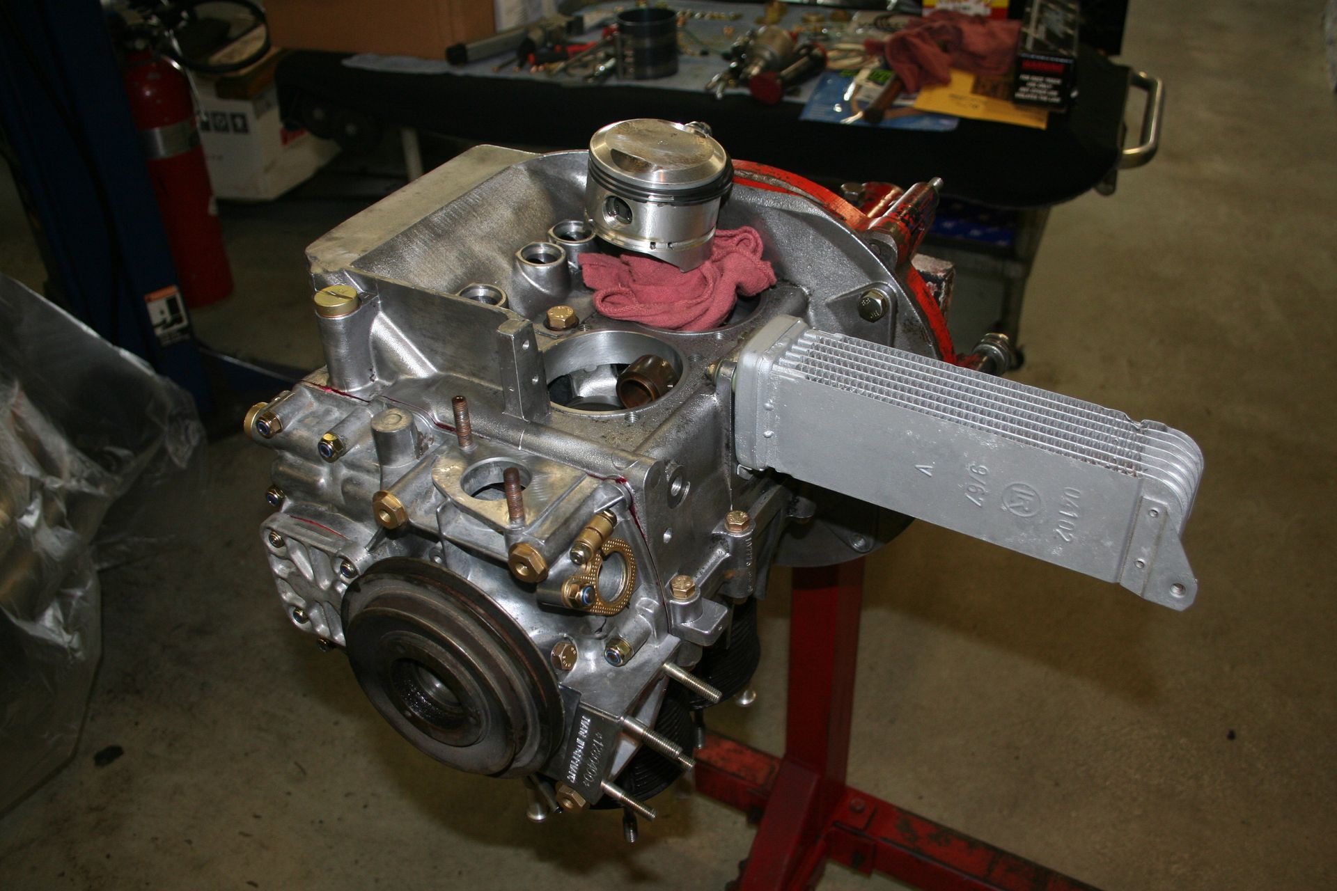Silver engine block with a piston exposed, on a stand with an oil cooler attached. Workshop setting. | Autobahn Performance Inc