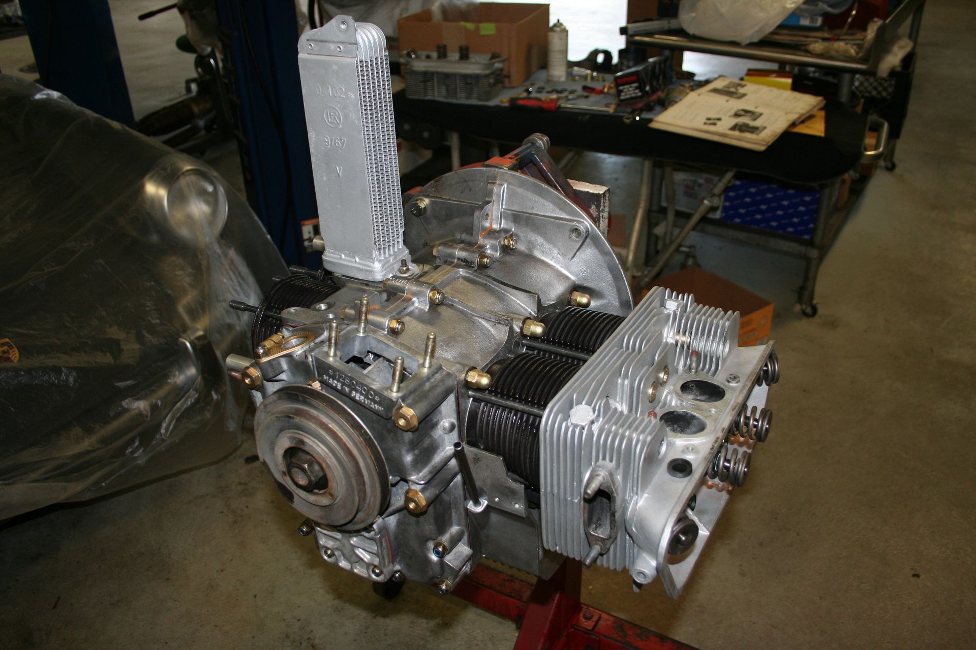 Aircraft engine, silver metal, with cooling fins and attached components, sitting on a red stand. Workshop setting. | Autobahn Performance Inc