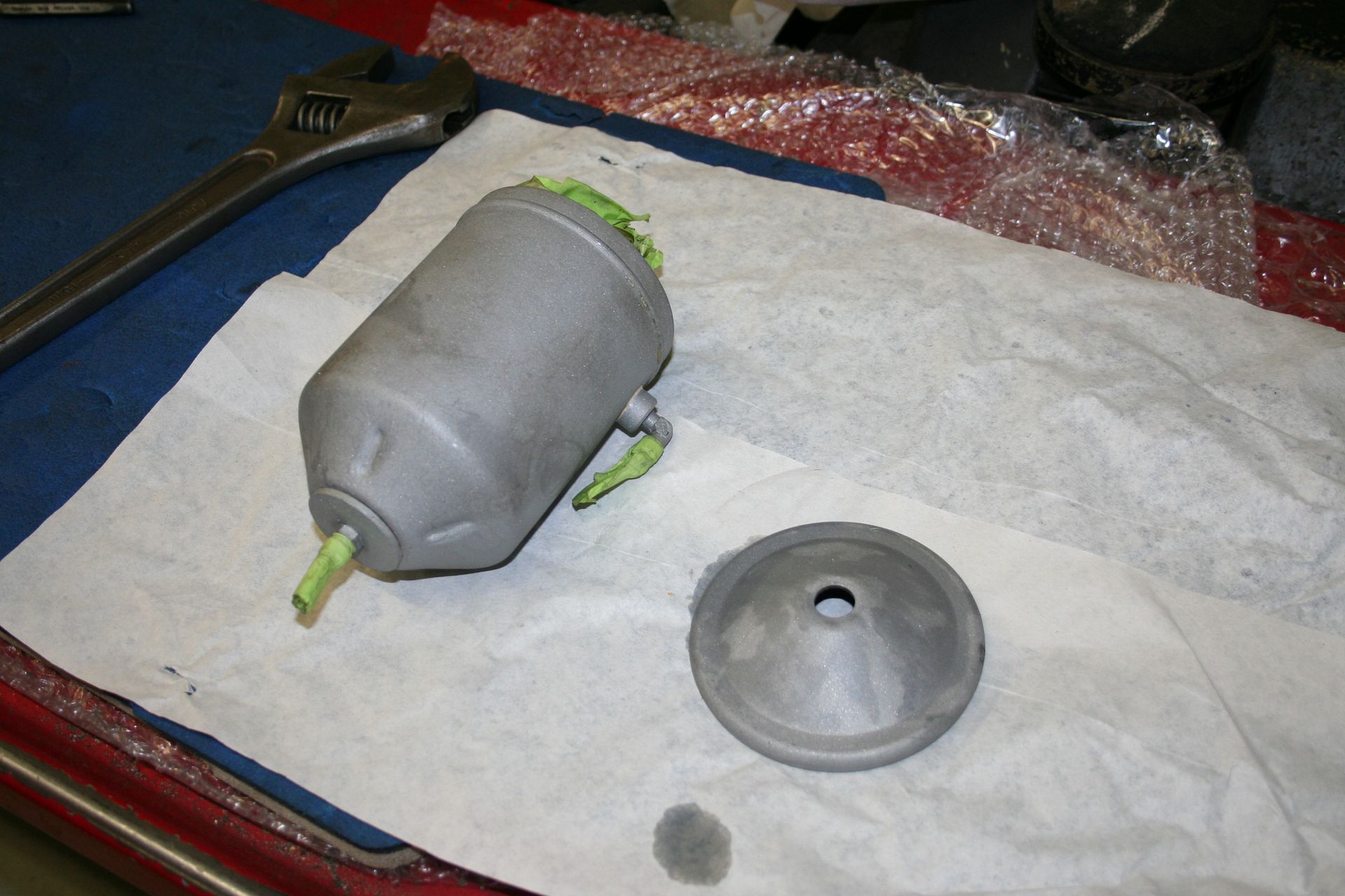 A disassembled gray metal car part on a white paper towel with an adjustable wrench in the background. | Autobahn Performance Inc