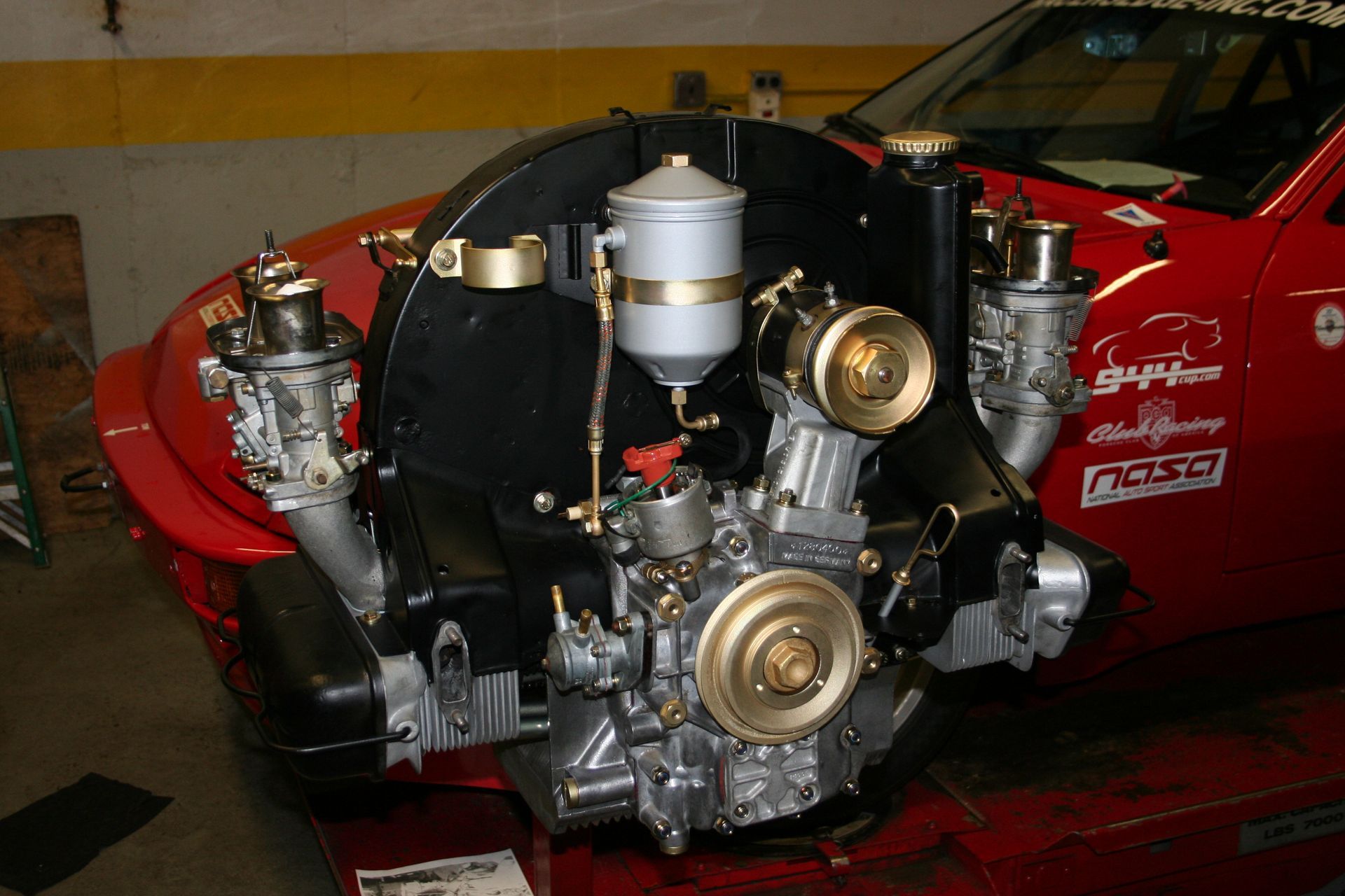 A black and silver car engine with gold accents. In a garage setting next to a red car. | Autobahn Performance Inc