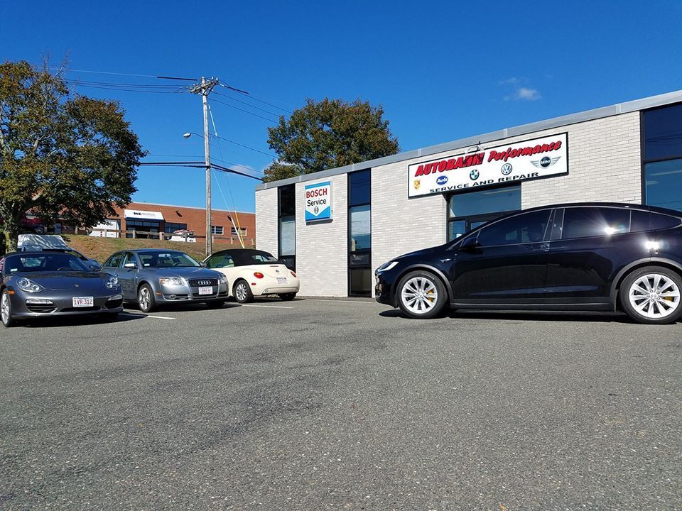 Cars parked in front of a grey auto repair shop under a clear blue sky. | Autobahn Performance Inc