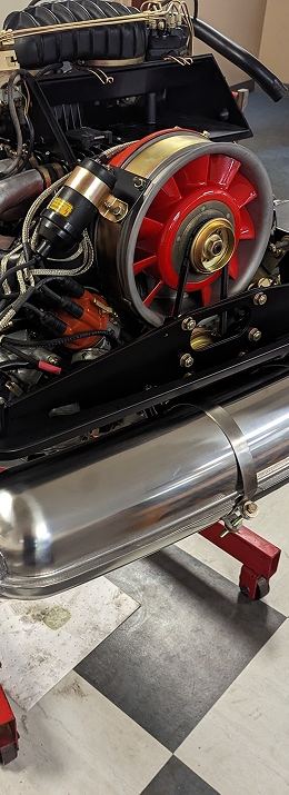 A car engine with a red fan and a silver exhaust. The engine is black with gold accents, on a checked floor. | Autobahn Performance Inc