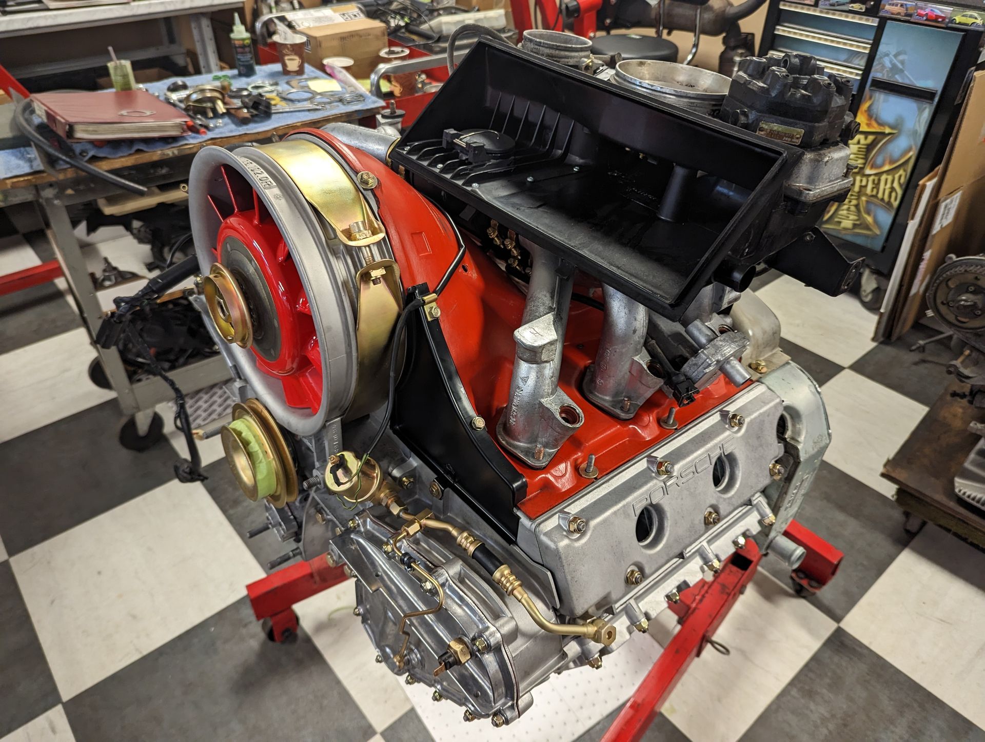 Red and silver engine on a stand in a workshop. Brass tubing, black airbox, and red fan visible. | Autobahn Performance Inc