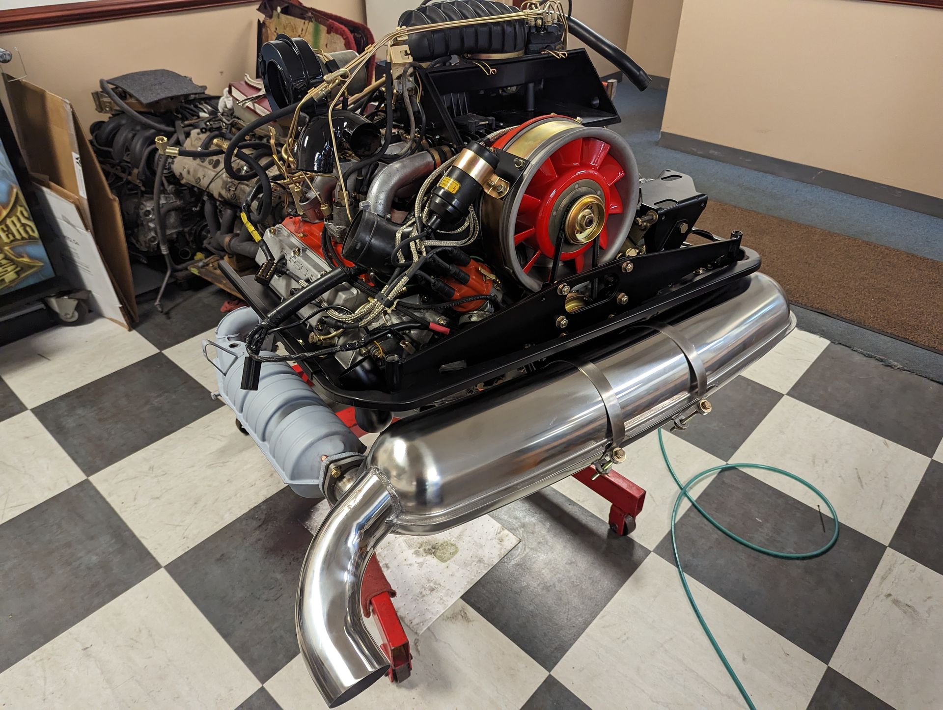 Porsche engine, partially disassembled, on a stand with a stainless steel muffler, red fan, and black wiring. | Autobahn Performance Inc