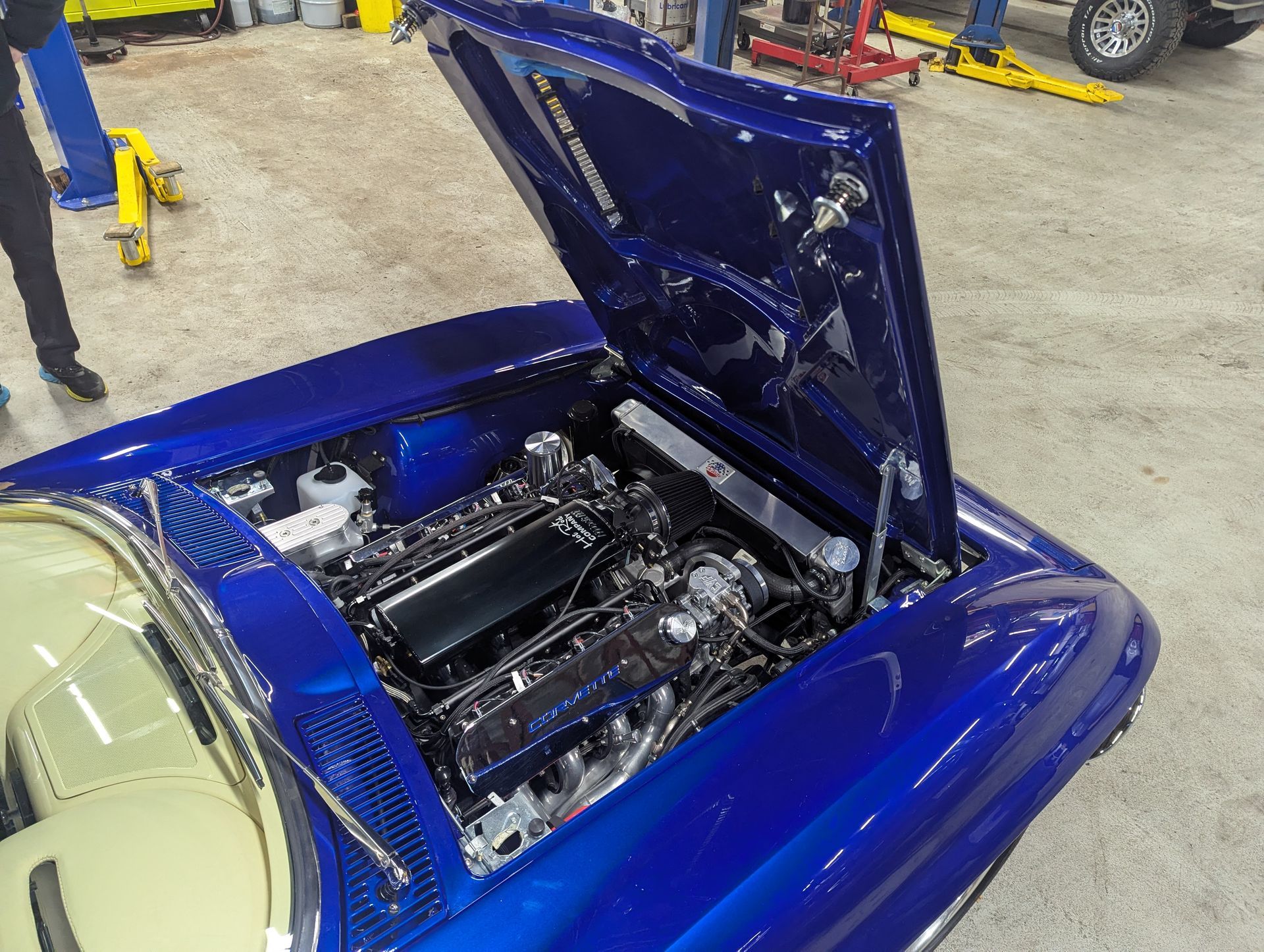 Blue classic car with open hood, shiny engine, in a garage. | Autobahn Performance Inc