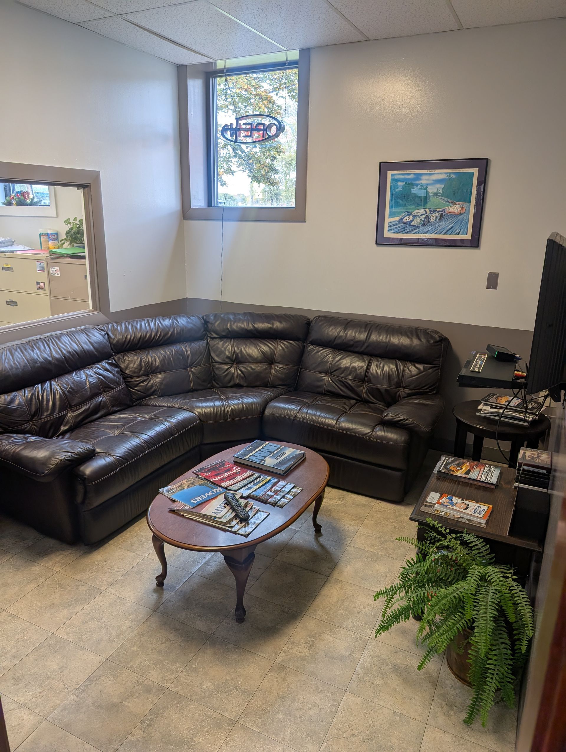 Waiting room with a dark leather sectional sofa, coffee table, and TV. | Autobahn Performance