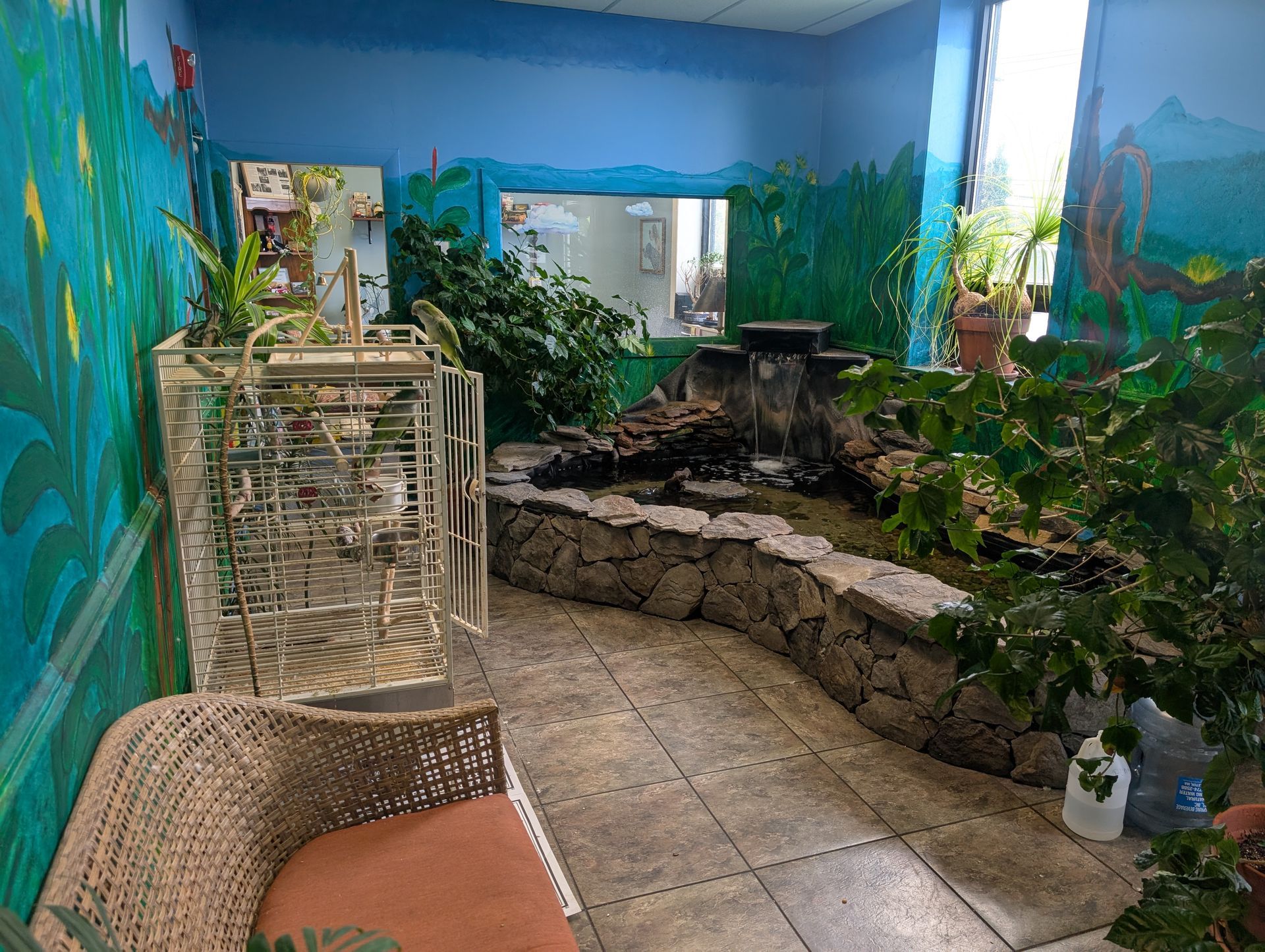 An indoor bird sanctuary with a small waterfall, plants, a cage, and a wicker chair. | Autobahn Performance