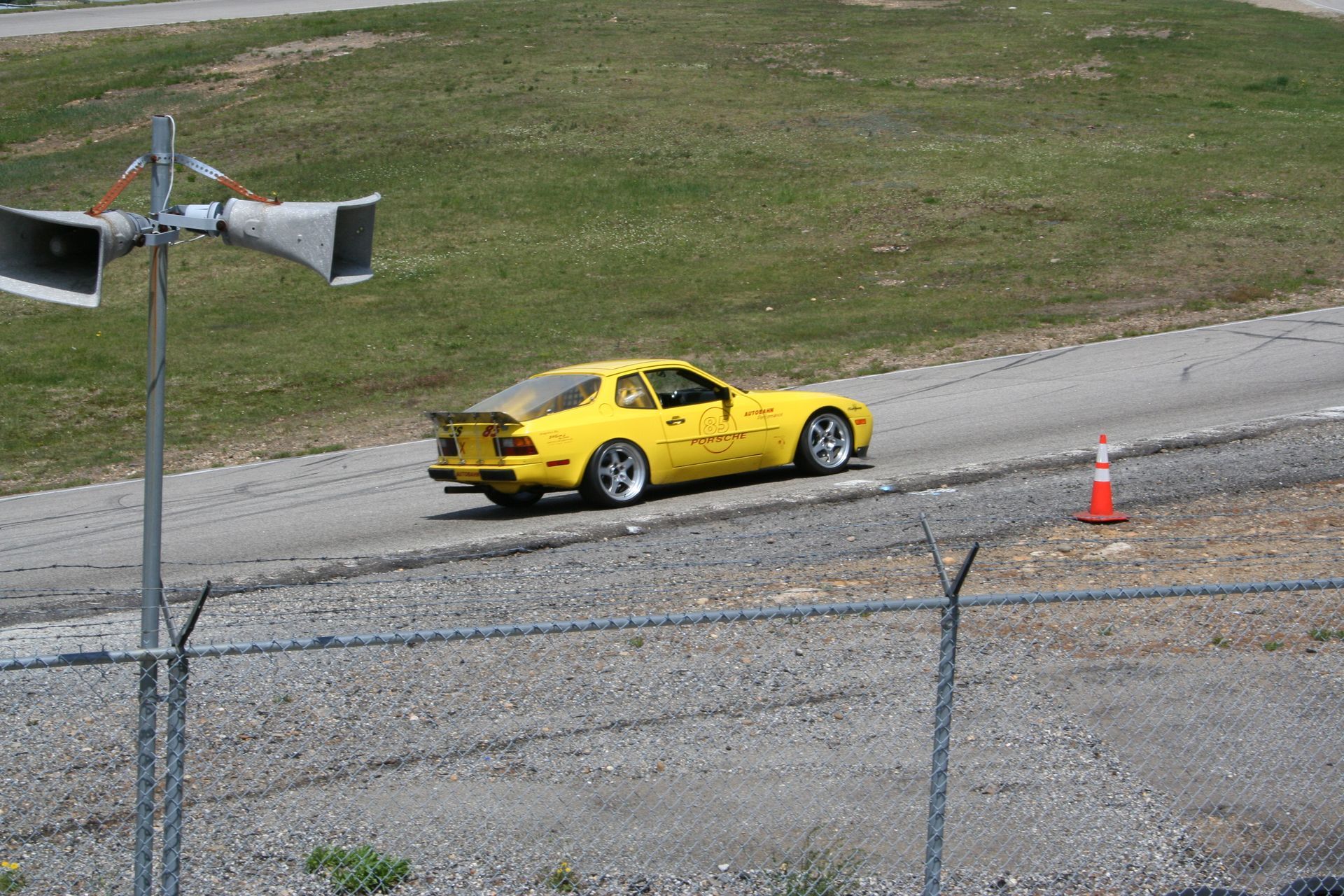 Yellow Porsche car driving on a paved road next to a grassy hill. | Autobahn Performance Inc