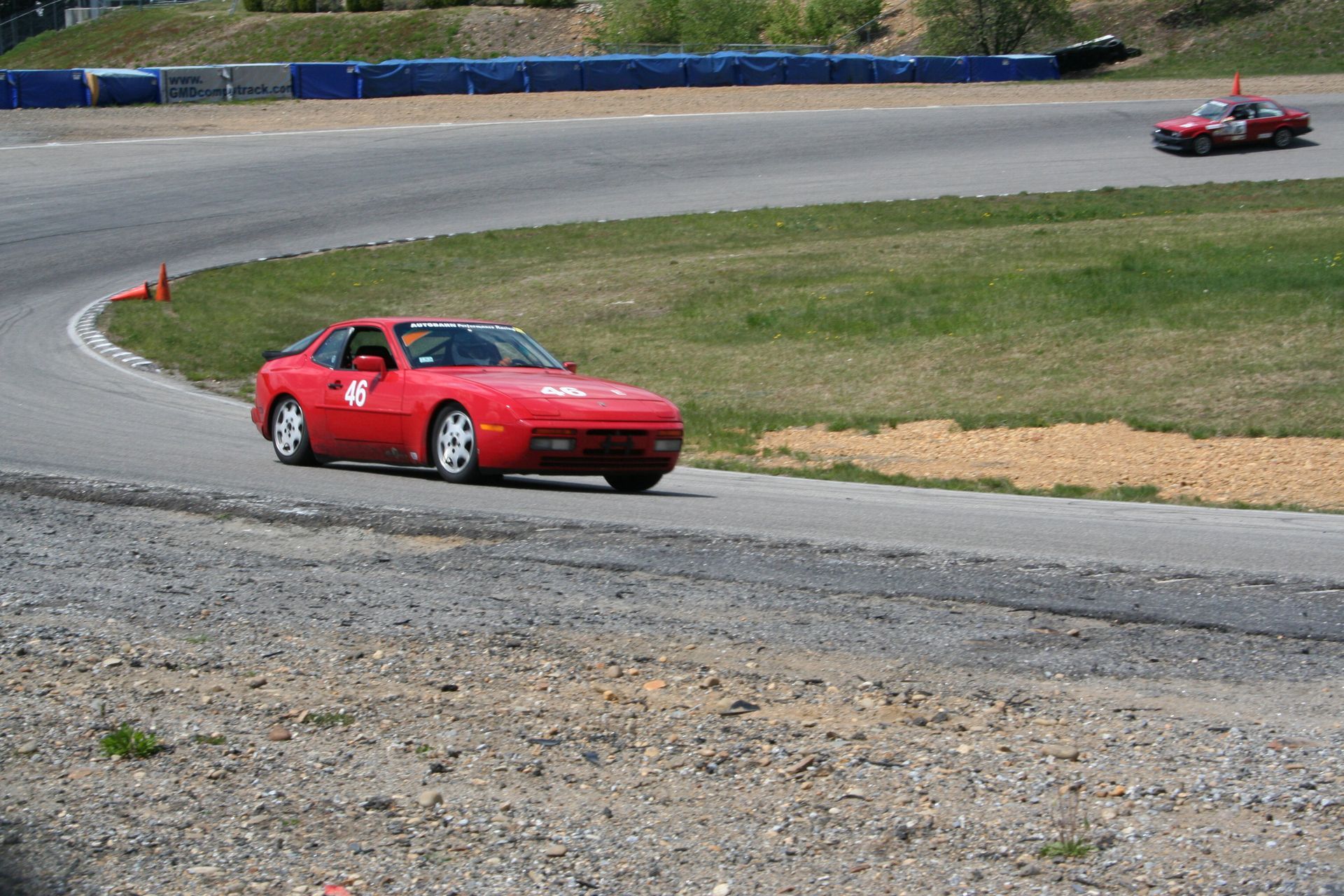 Red sports car on racetrack, cornering with another car visible further away. | Autobahn Performance Inc