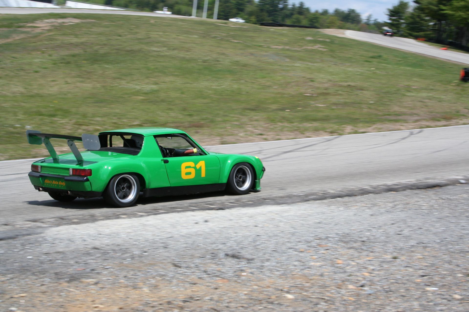 Green race car #61 on a track, large spoiler, grass hillside in background. | Autobahn Performance Inc