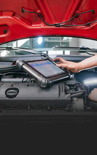 A mechanic using a diagnostic tool on a car engine under the open hood; red car. | Autobahn Performance Inc