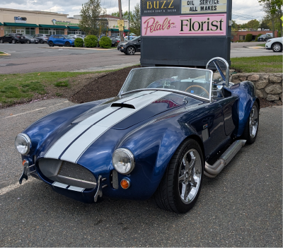 Blue Shelby Cobra roadster with white stripes parked in front of a florist. | Autobahn Performance Inc
