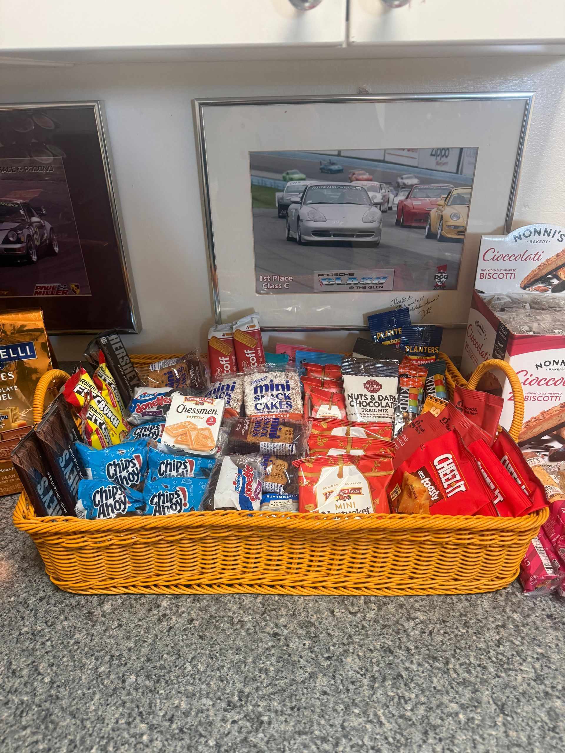 A yellow wicker basket filled with various snacks on a countertop, with framed pictures in the background. | Autobahn Performance