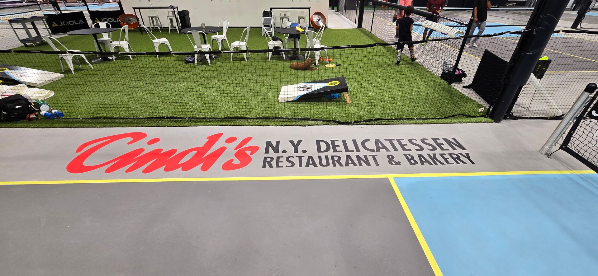 A basketball court with the name cindy 's n.y. delicatessen restaurant and bakery painted on it.
