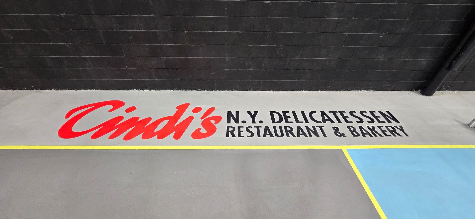 A sign for cindi 's n.y. delicatessen restaurant and bakery is painted on the floor.