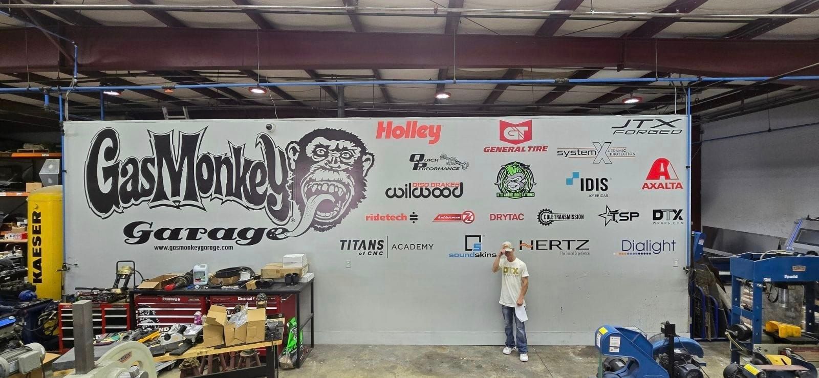 A man is standing in front of a large wall that says gas monkey garage.
