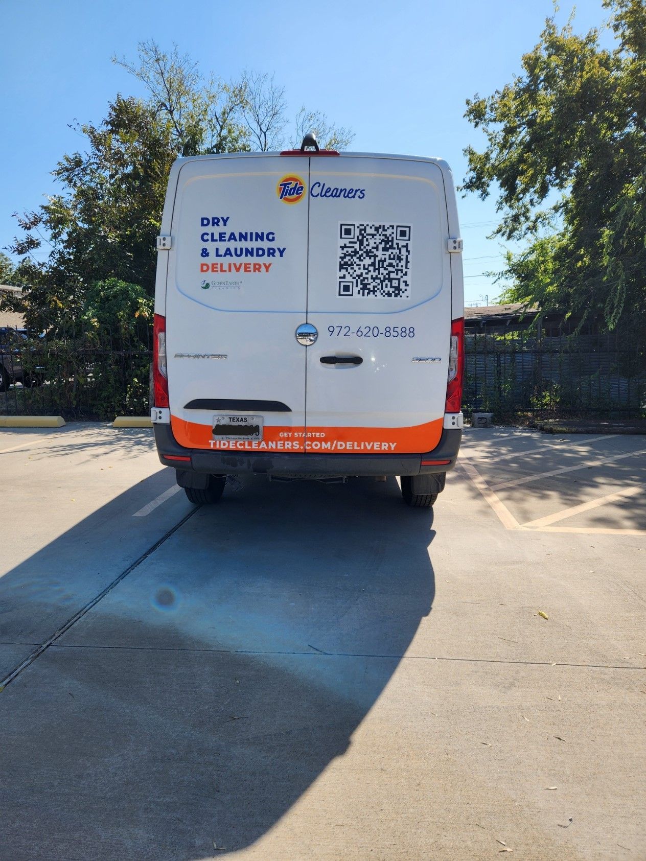 A white van with a qr code on the back is parked in a parking lot.