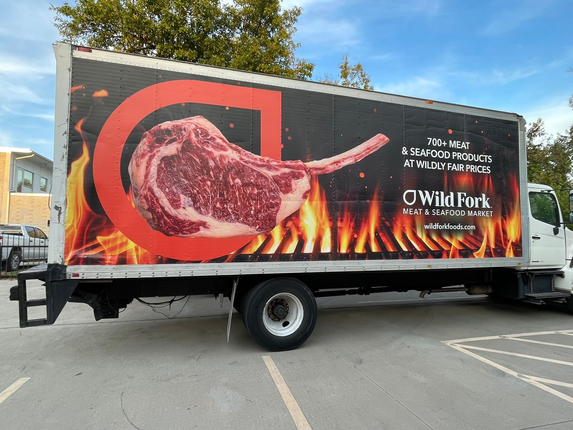 A truck with a picture of a steak on the side is parked in a parking lot.