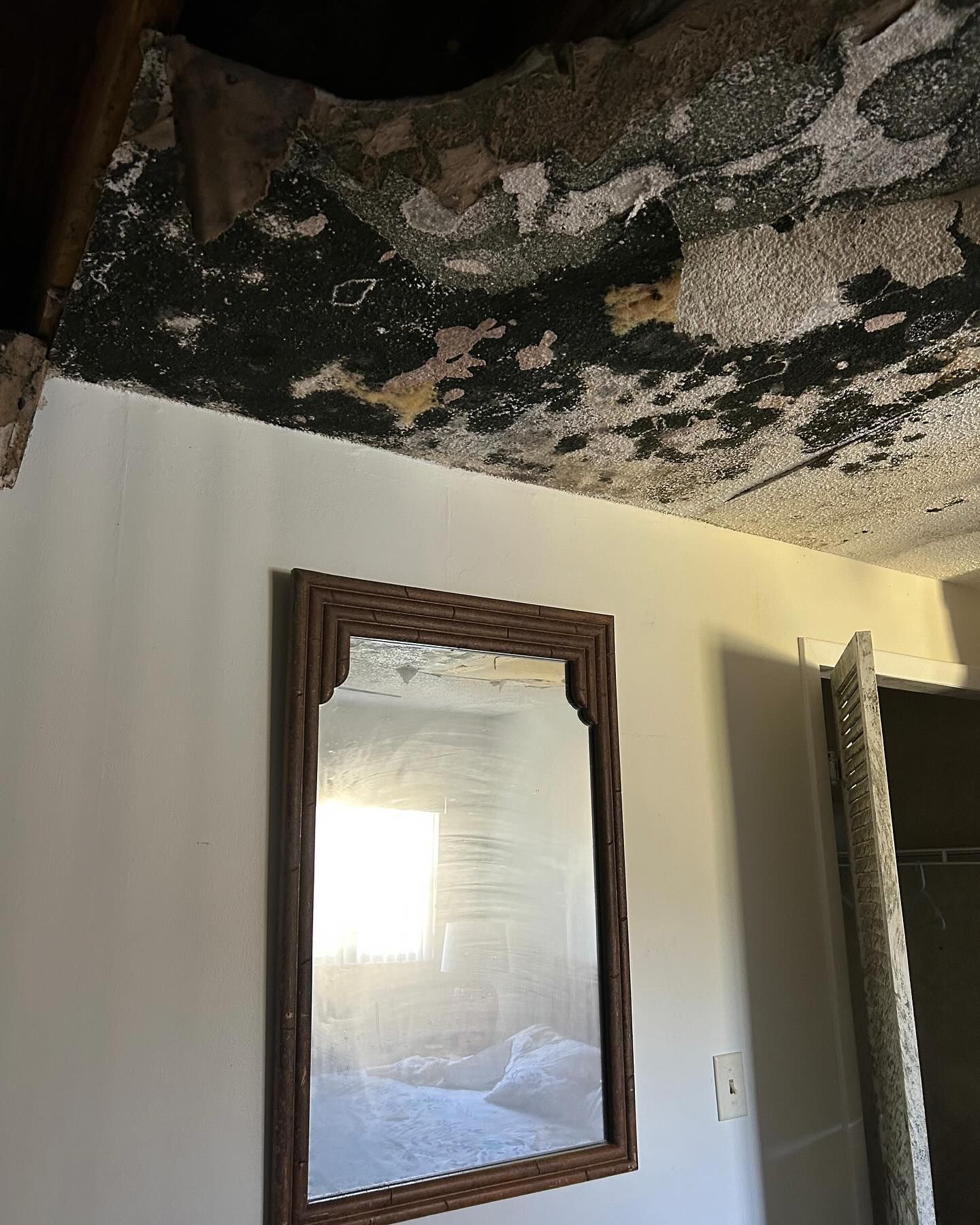 A mirror is hanging on a wall in a room with a damaged ceiling
