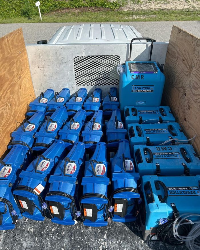 A cargo bed loaded with multiple blue industrial-style portable fans and dehumidifiers for water damage restoration.
